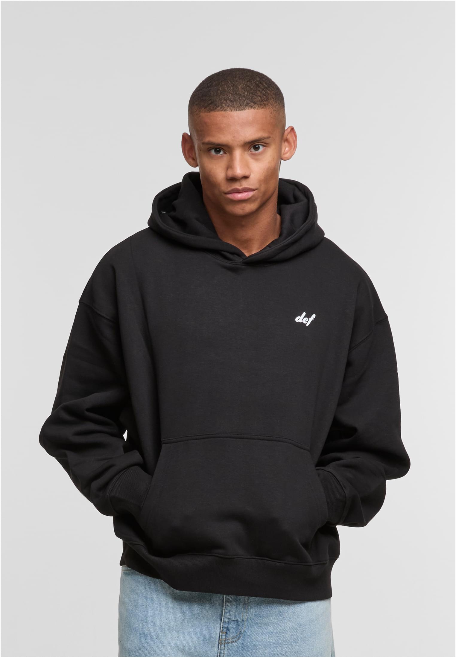 En man visar framsidan av den svarta huvtröjan DEF VISIONS.