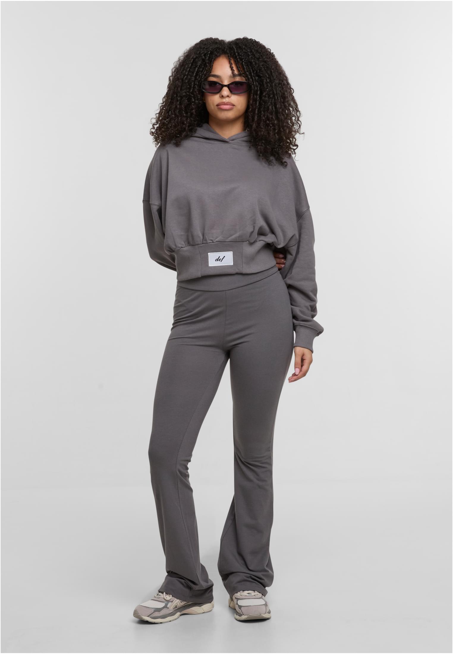 En kvinna visar framsidan av en grå, croppad hoodie och matchande utsvängda byxor från DEF.