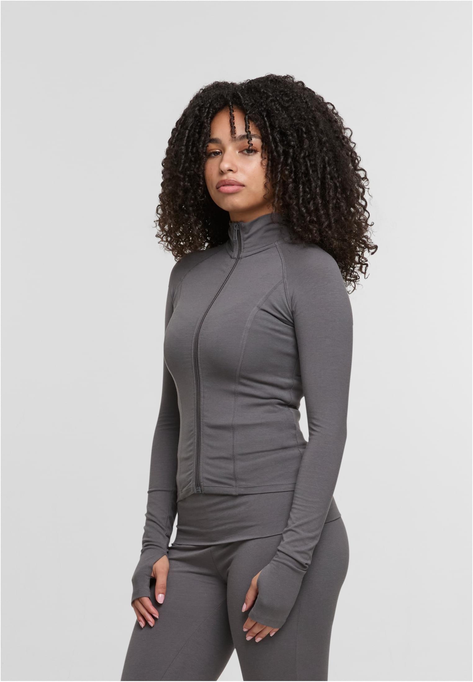 En kvinna visar framsidan av den gråa DEF GYM Track Jacket.