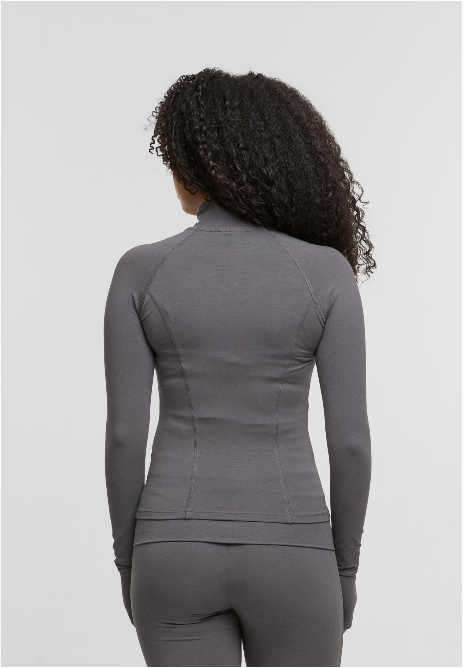En kvinna visar baksidan av en grå, långärmad och figurnära träningsjacka.