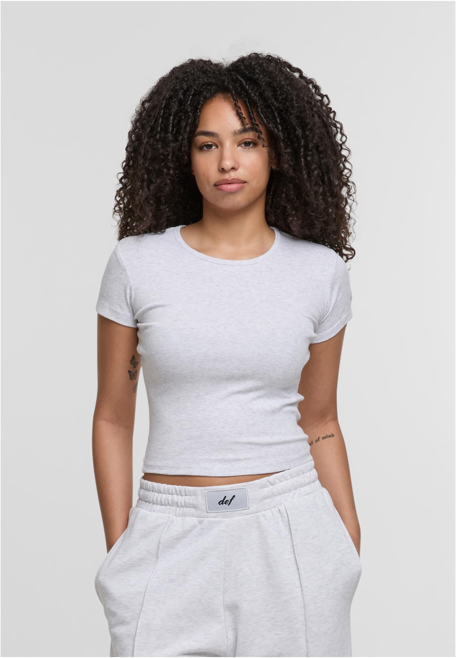 En kvinna visar framsidan av en ljusgrå, åtsittande DEF Relax T-shirt.