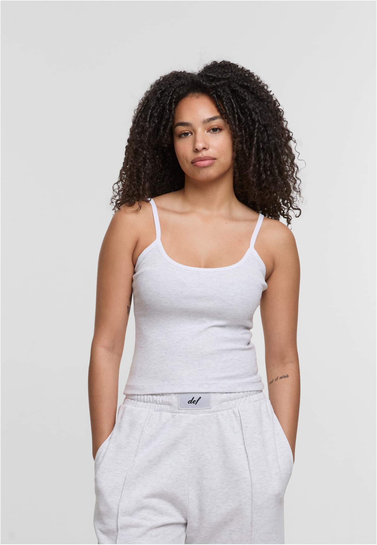 En kvinna visar framsidan av ett ljusgrått, ribbat linne från DEF.