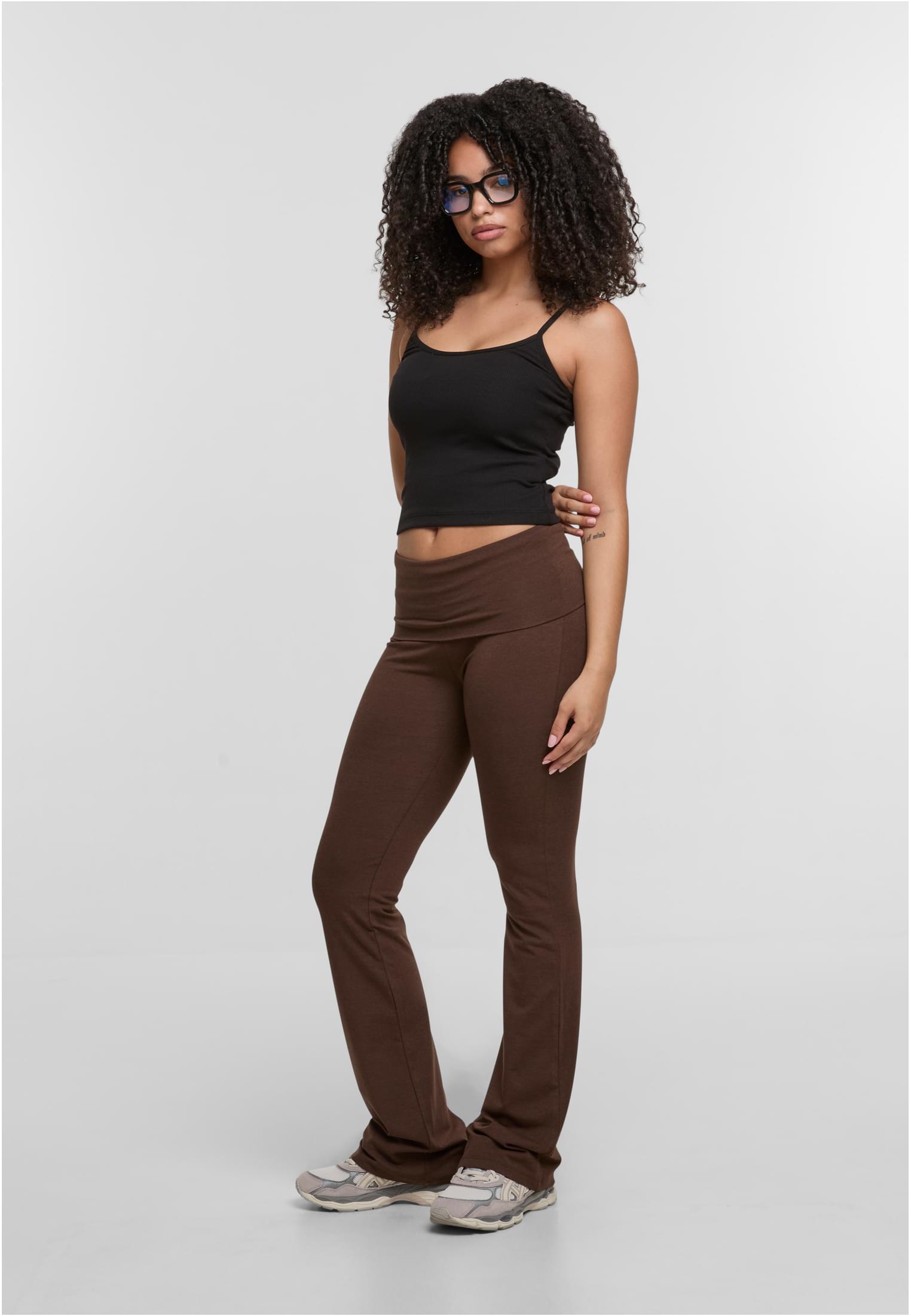 En kvinna poserar från sidan iklädd ett svart linne från DEF RELAX Tops och bruna byxor.