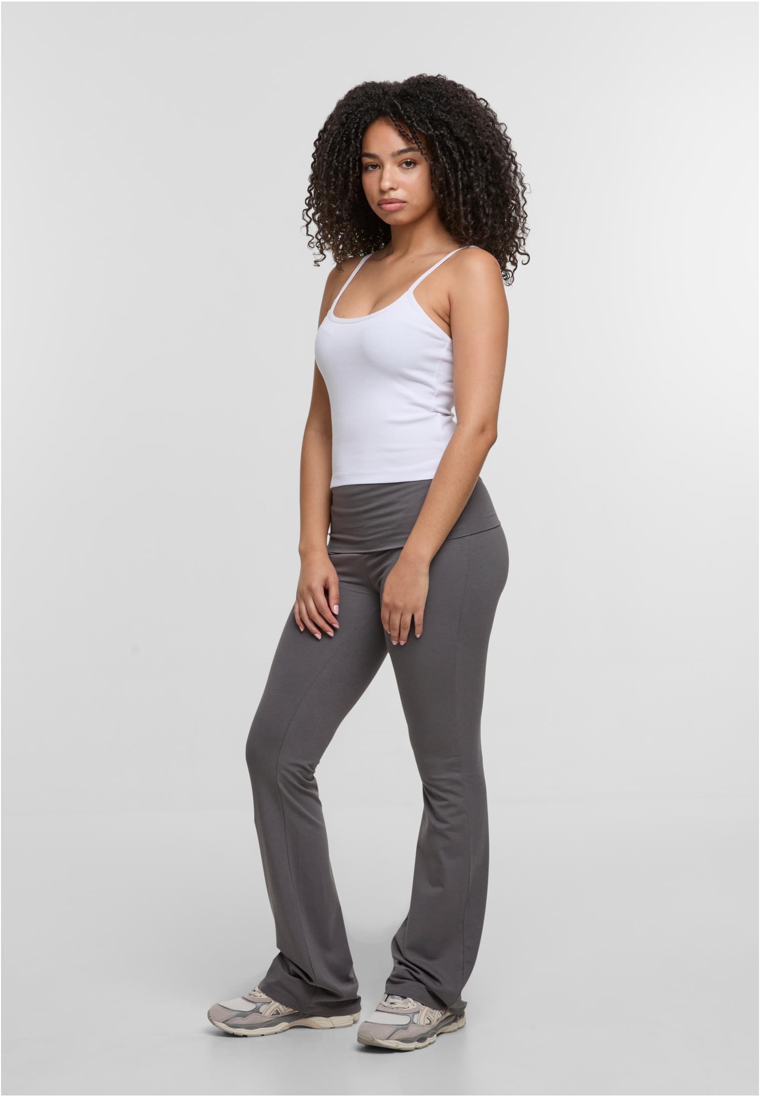 En kvinna poserar i ett vitt linne från DEF RELAX Tops och grå utsvängda byxor.