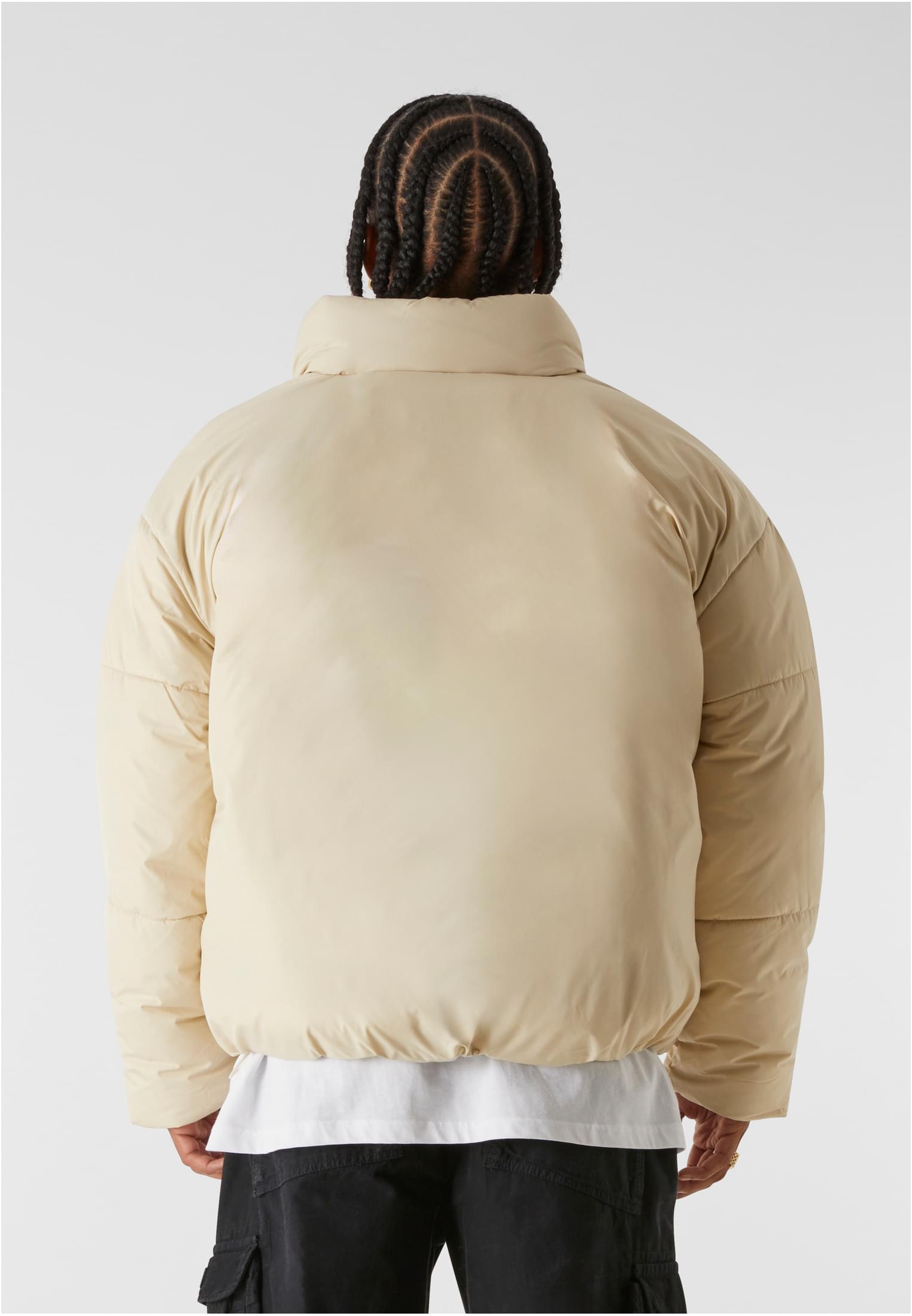 En man visar baksidan av den beiga MJG Puffer Jacket.