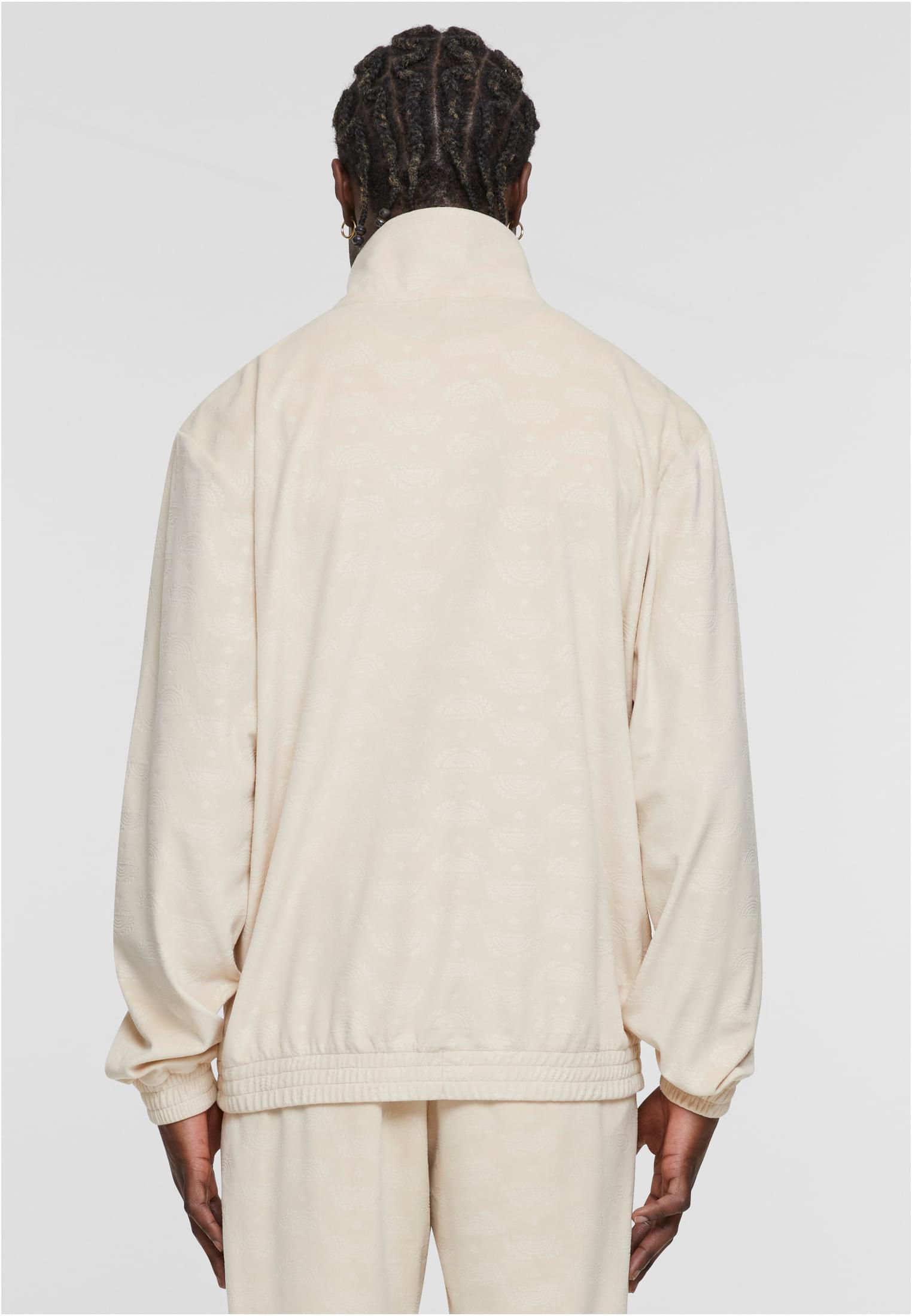 En man, sedd bakifrån, bär en beige velourjacka med ett heltäckande logotypmönster.