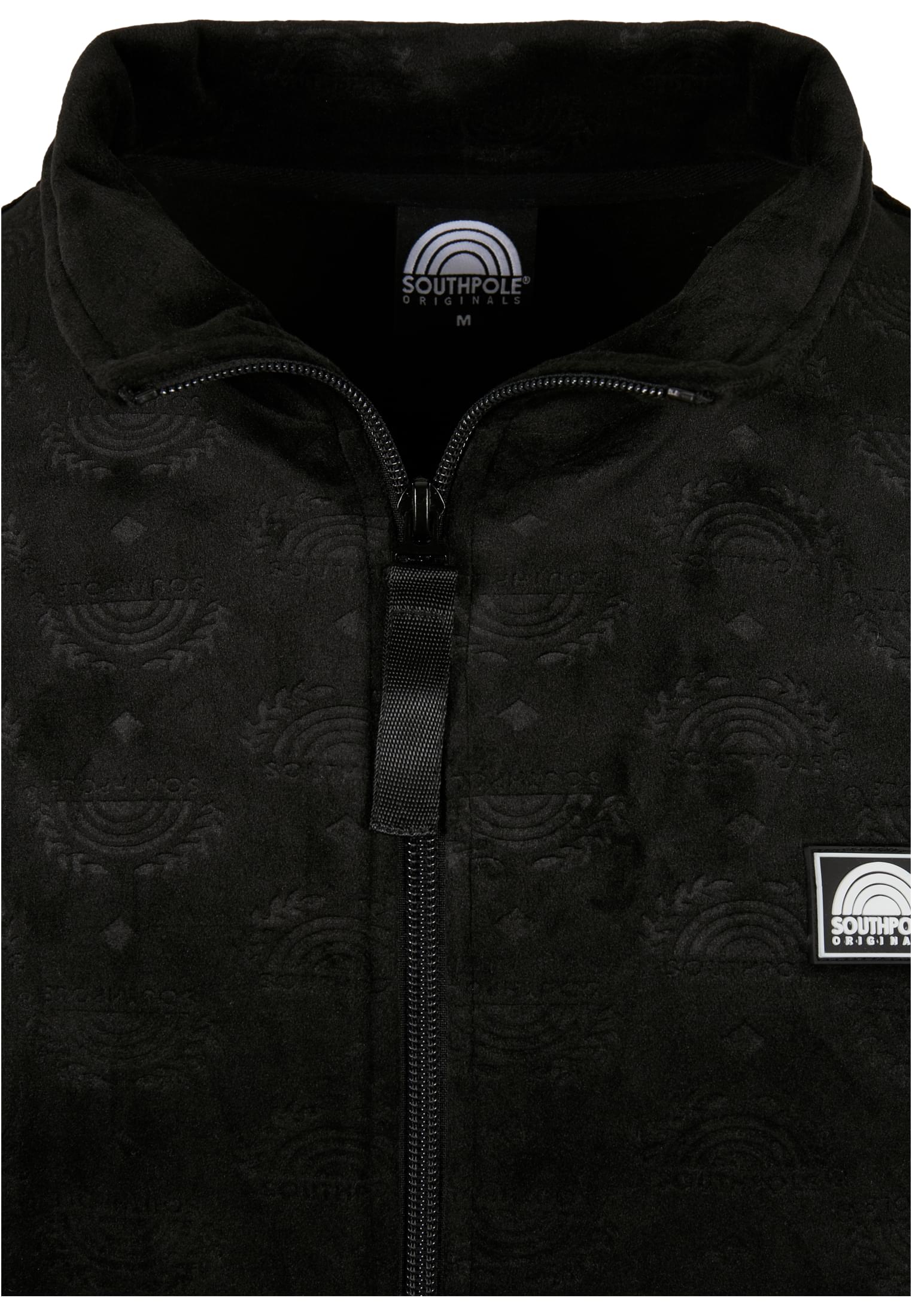 Närbild på den svarta SP AOP Velour Jackan som visar detaljer som dragkedjan, kragen och det präglade logomönstret i tyget.