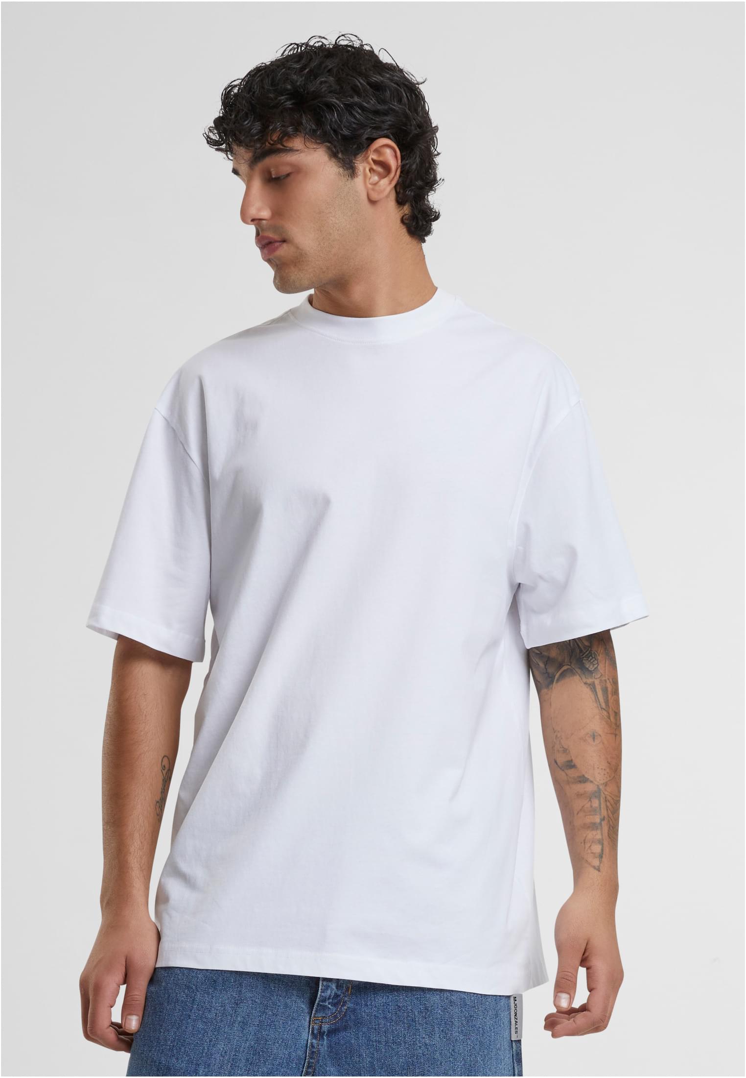 Manlig modell med tatueringar på armarna bär en vit t-shirt med extra lång passform.