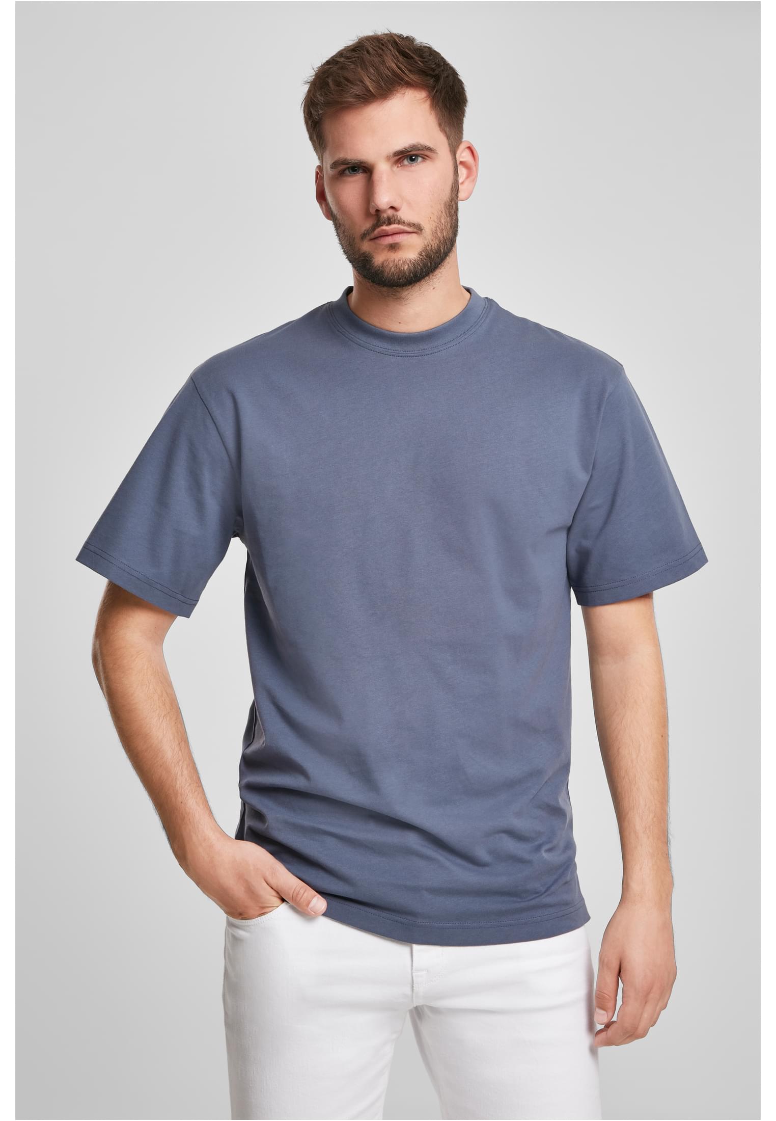 Manlig modell som bär en dovt blå Tall Tee t-shirt och vita byxor mot en grå bakgrund.