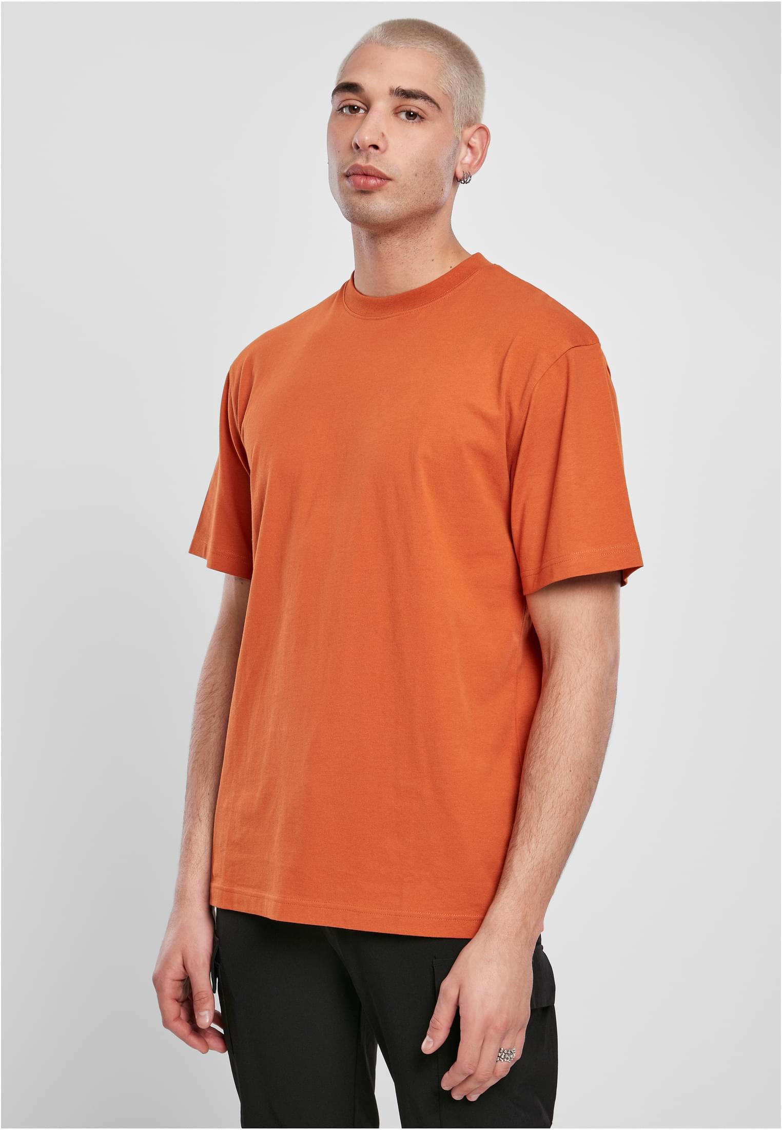 En manlig modell som bär den orange t-shirten UC Tall Tee mot en ljusgrå bakgrund.
