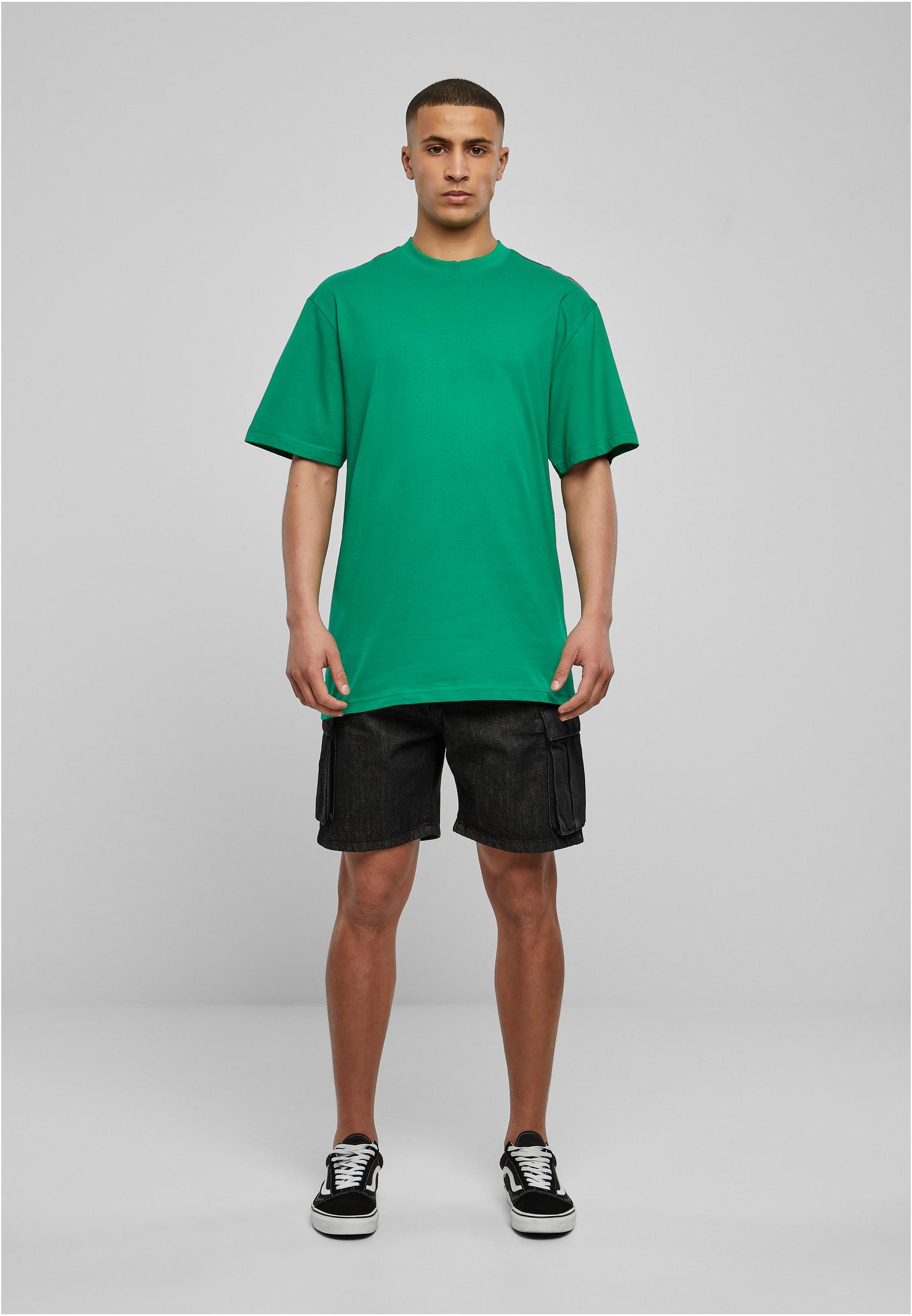 Frontbild på en man som bär en grön Tall Tee, svarta shorts och sneakers.