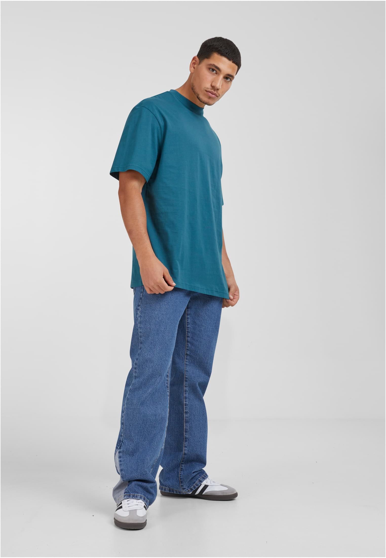 Manlig modell som bär en frostmint-färgad Tall Tee med extra lång passform, blåa jeans och sneakers, fotograferad mot en vit bakgrund.