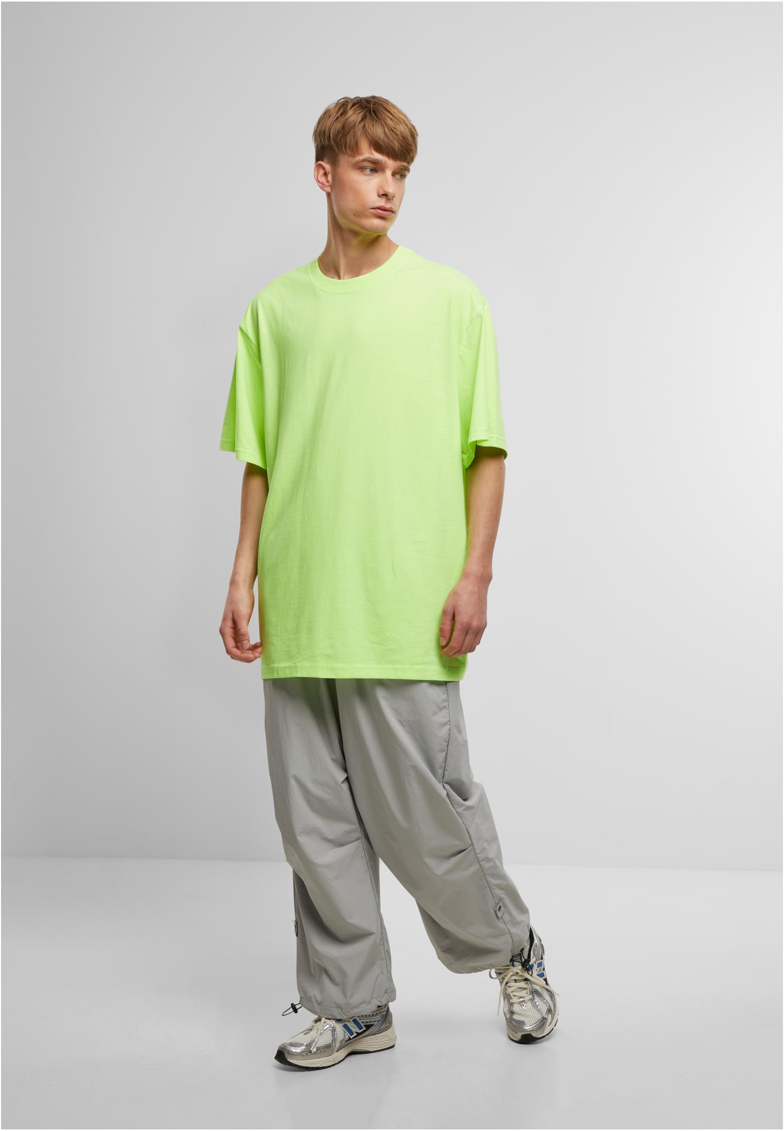 Manlig modell i en neongrön, extra lång t-shirt och vida grå byxor.