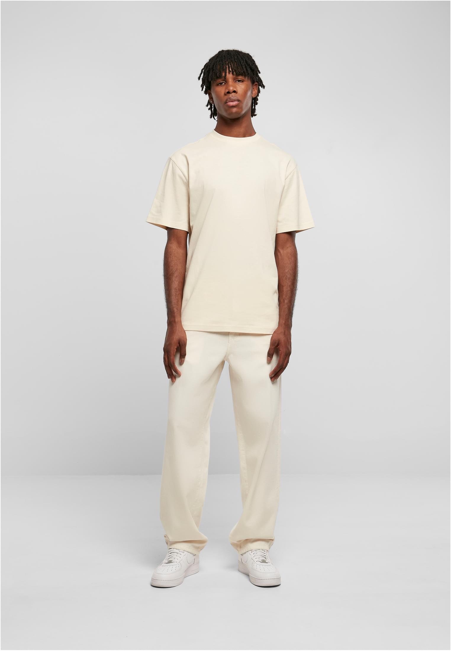 Manlig modell i helfigur som bär en ljus Tall Tee från Urban Classics med extra lång passform, tillsammans med matchande ljusa byxor och vita sneakers.