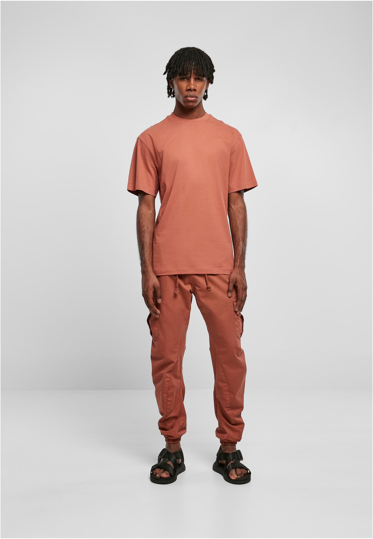 Manlig modell i helfigur som bär en rostfärgad Tall Tee med extra lång passform och matchande byxor, fotograferad framifrån mot en ljusgrå bakgrund.