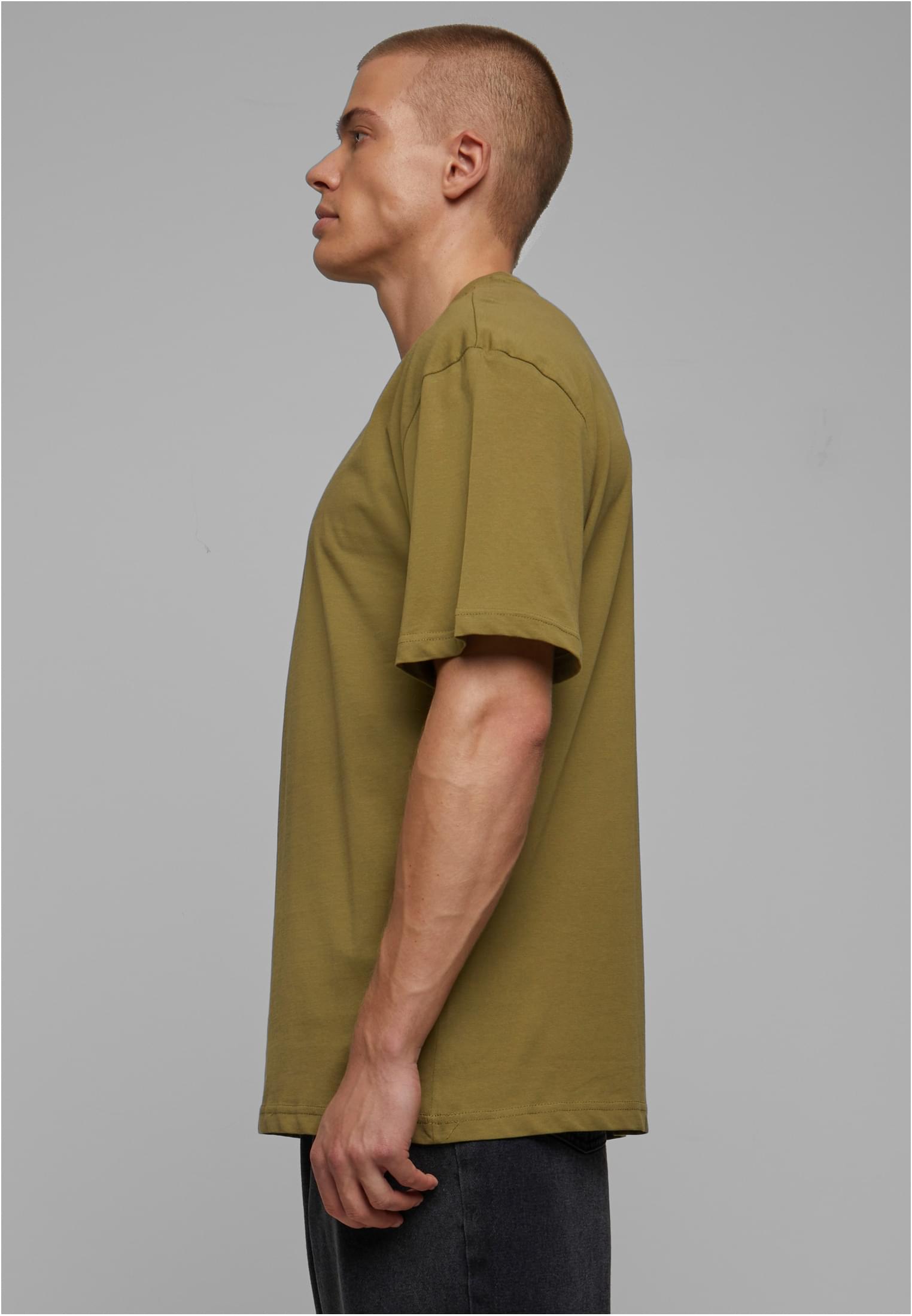 Manlig modell i profil som bär en olivgrön t-shirt med extra lång passform, en så kallad Tall Tee, mot en ljusgrå bakgrund.