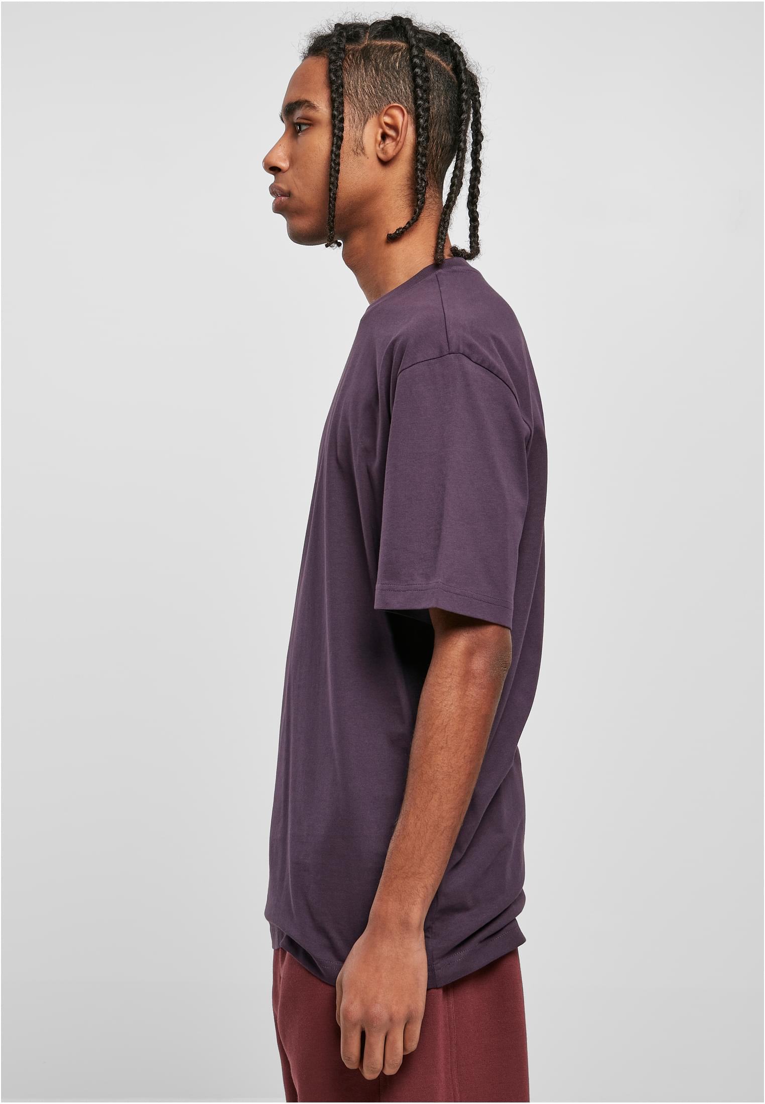 Sidovy av en man med flätat hår som bär en mörklila Tall Tee från Urban Classics.