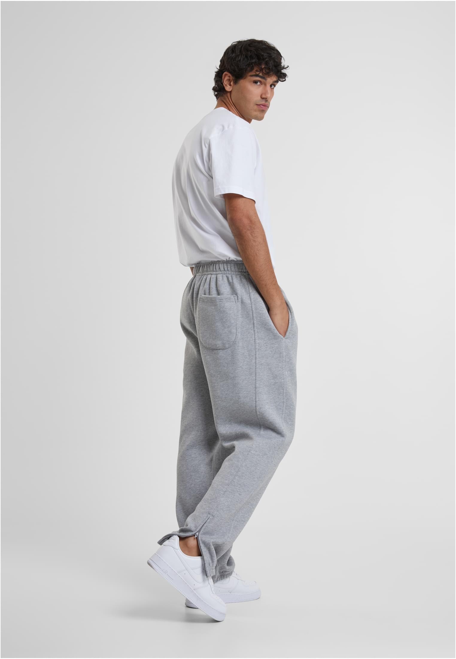 En man poserar från sidan i gråa sweatpants och en vit t-shirt.