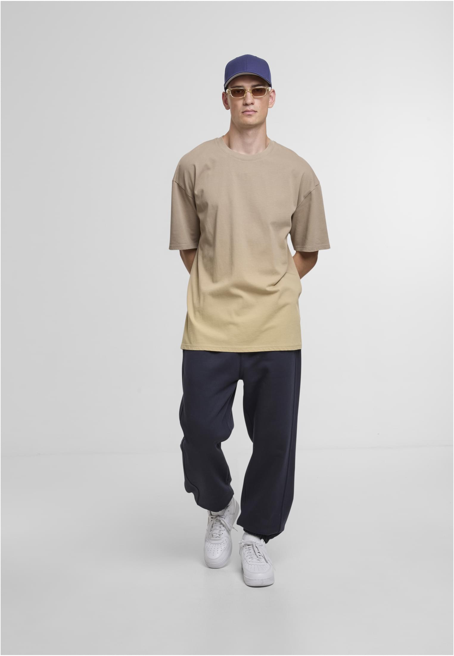 Man klädd i mörkblå sweatpants, en ledig beige t-shirt och en blå keps.