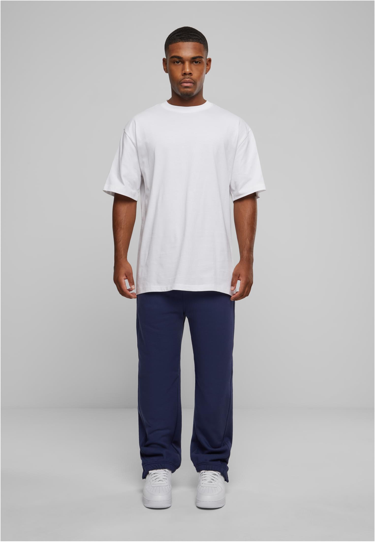 En manlig modell bär ett par mörkblå UC Sweatpants med en vit T-shirt och vita sneakers.