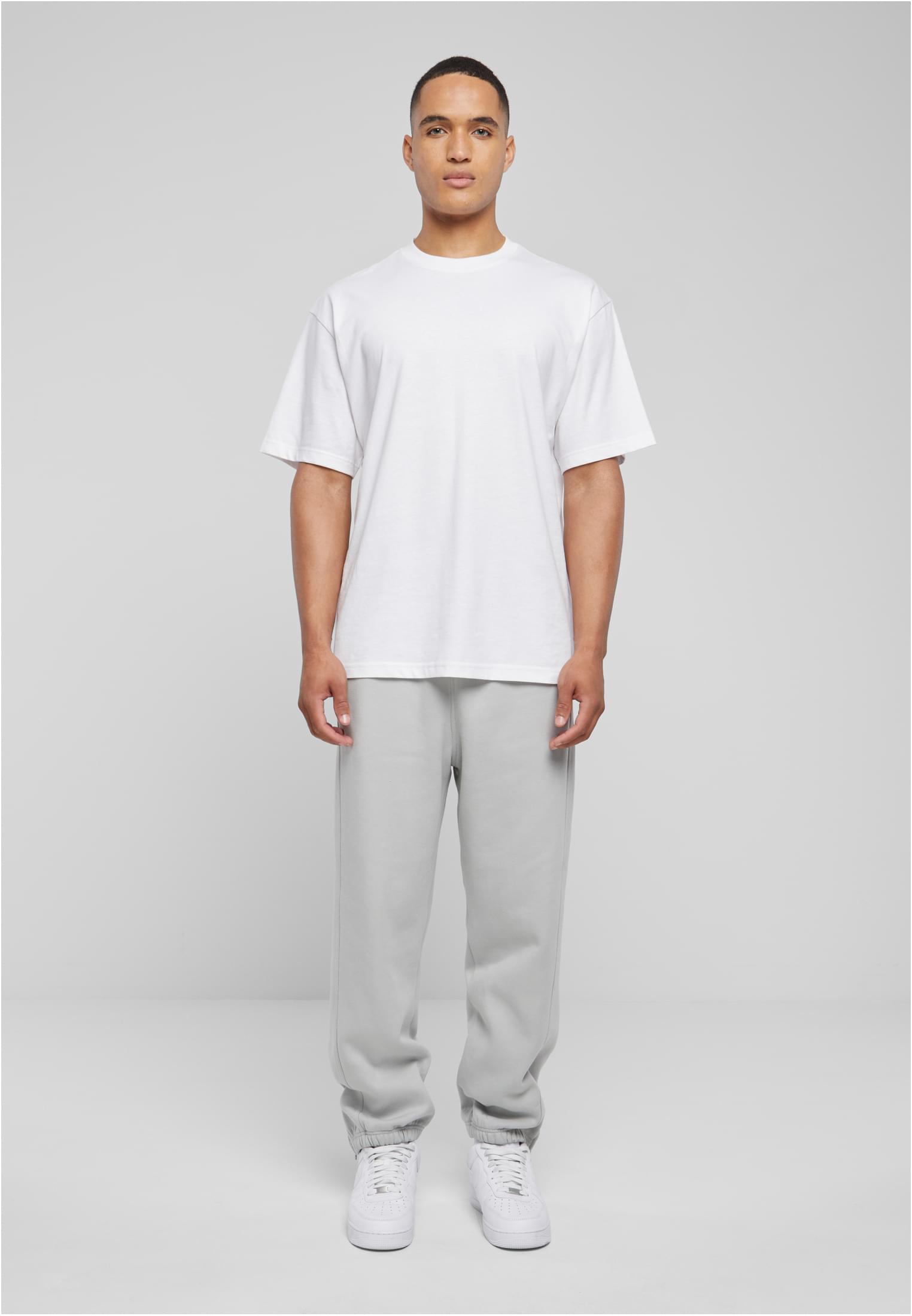 Helkroppsbild av en man som bär ljusgrå UC Sweatpants och en vit t-shirt mot en grå bakgrund.