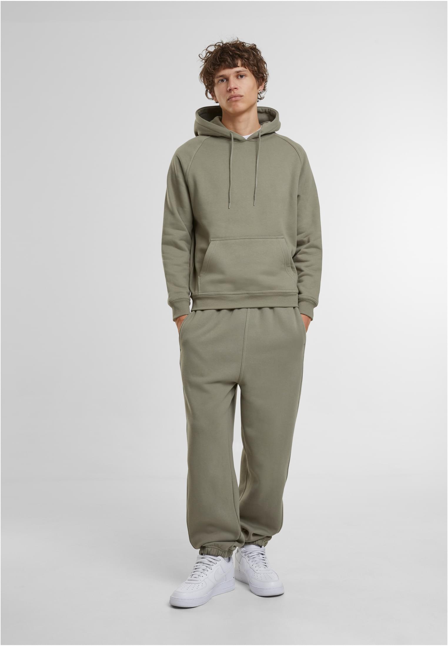 En manlig modell som bär ett matchande grönt set bestående av UC Sweatpants och en huvtröja, med vita sneakers.