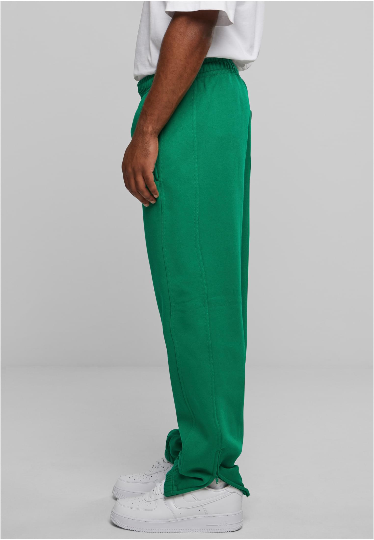 Modell från sidan i gröna sweatpants med dragkedja vid ankeln och vita sneakers.