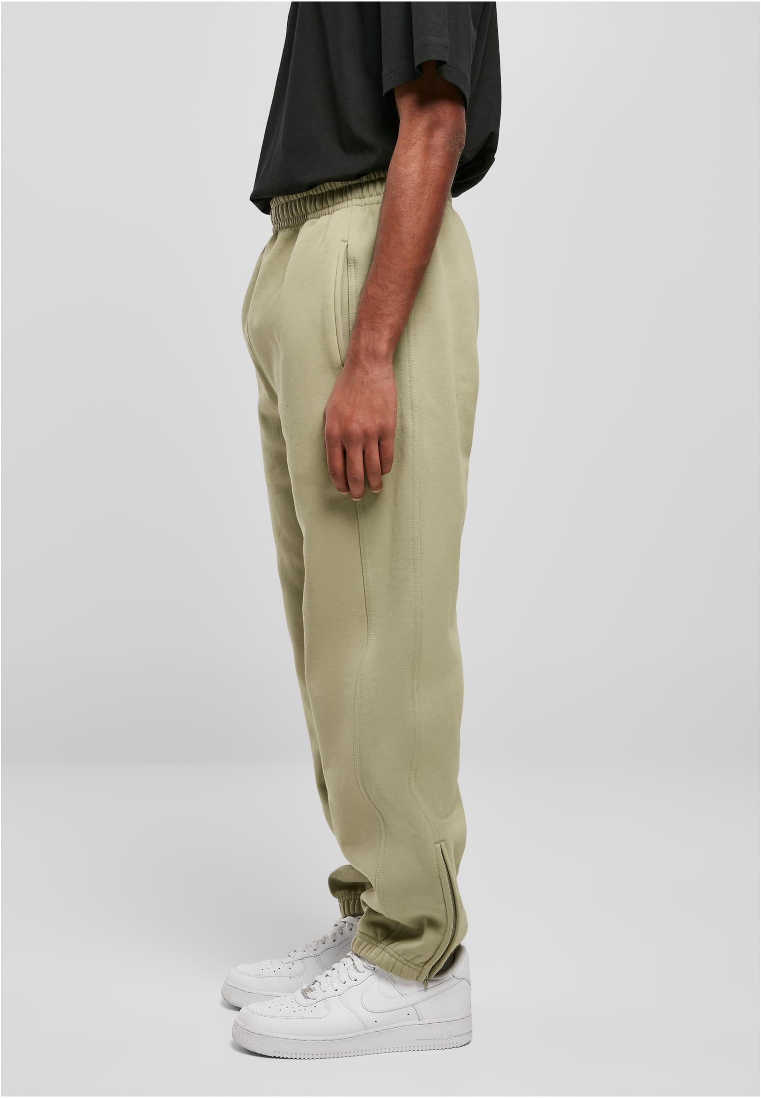 Sidoprofil av en man som bär ljusgröna UC Sweatpants med en svart t-shirt och vita sneakers mot en grå bakgrund.