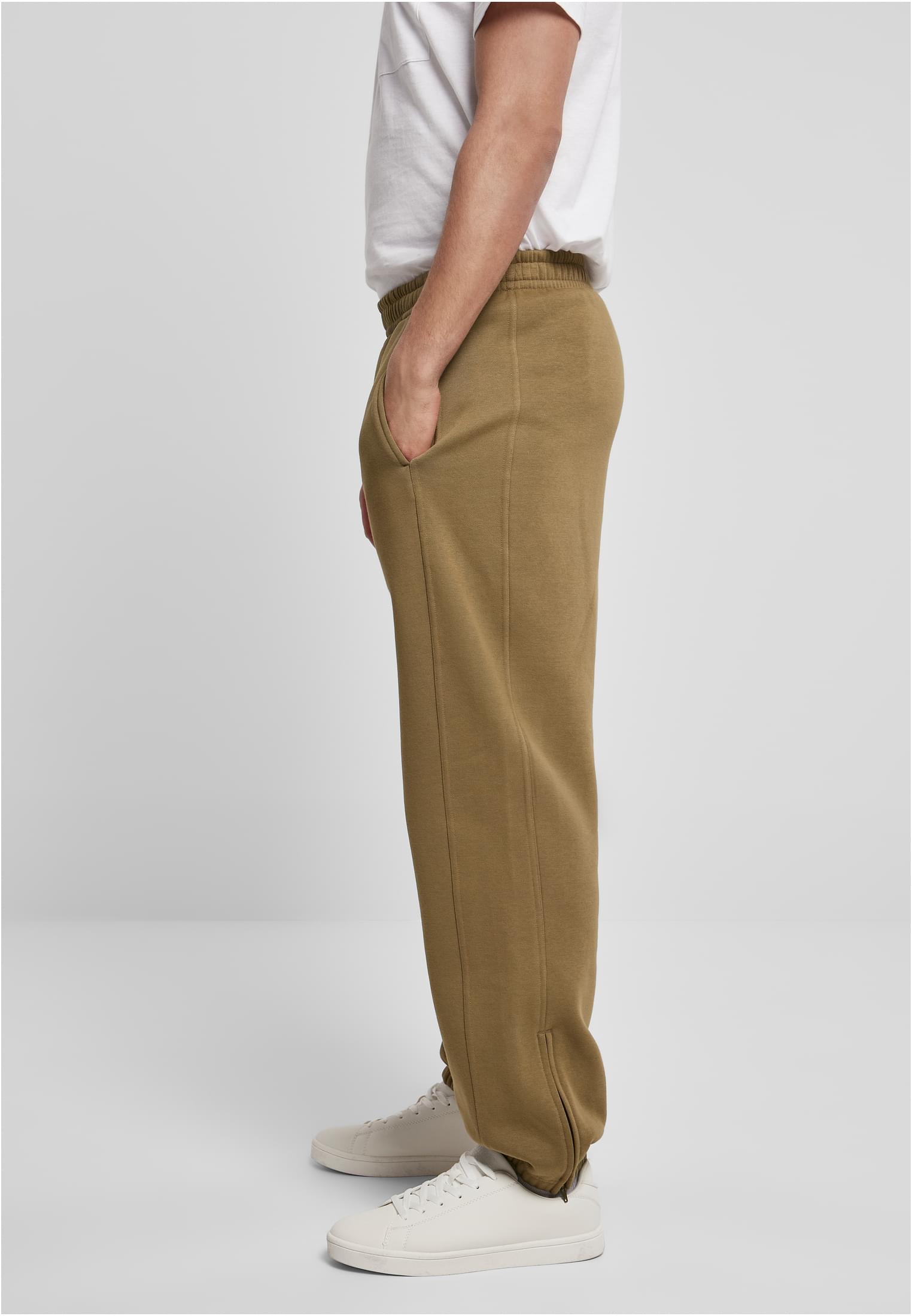 Sidoprofil av en man som bär olivgröna UC Sweatpants, en vit t-shirt och vita sneakers.