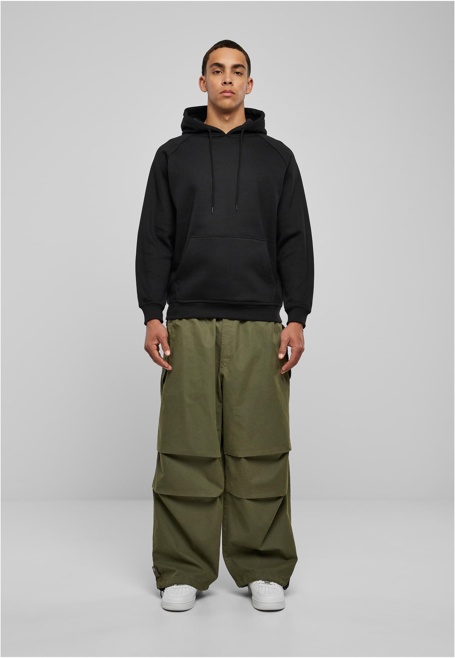 Manlig modell sedd framifrån, iklädd en svart luvtröja, olivgröna cargobyxor och vita sneakers.