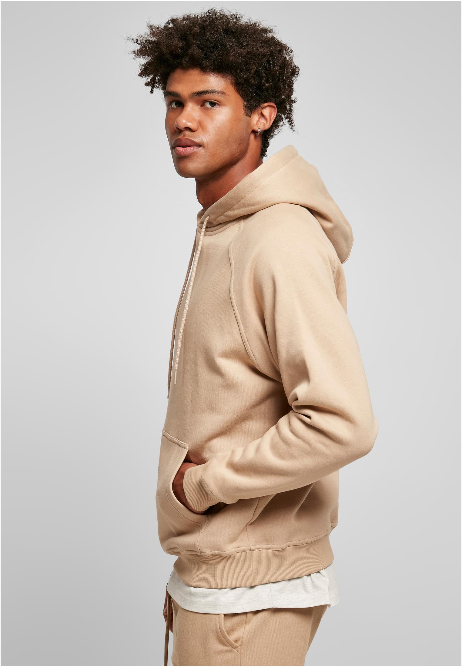Sidoprofil av en manlig modell som bär en beige UC Blank Hoody med handen i kängurufickan.