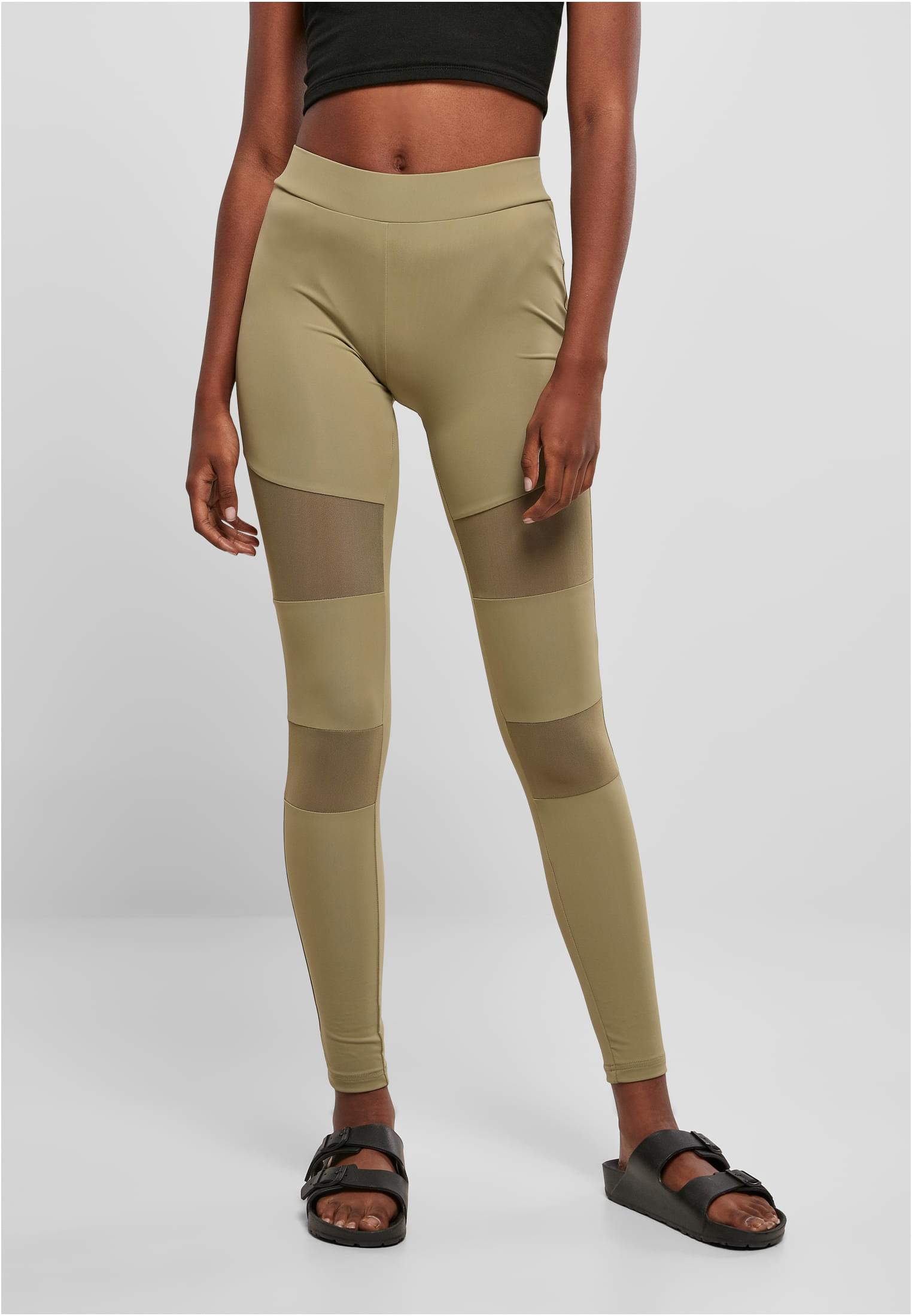 Framsida av en kvinna som bär varmgrå Ladies Tech Mesh Leggings med genomskinliga meshpaneler på låren och smalbenen.