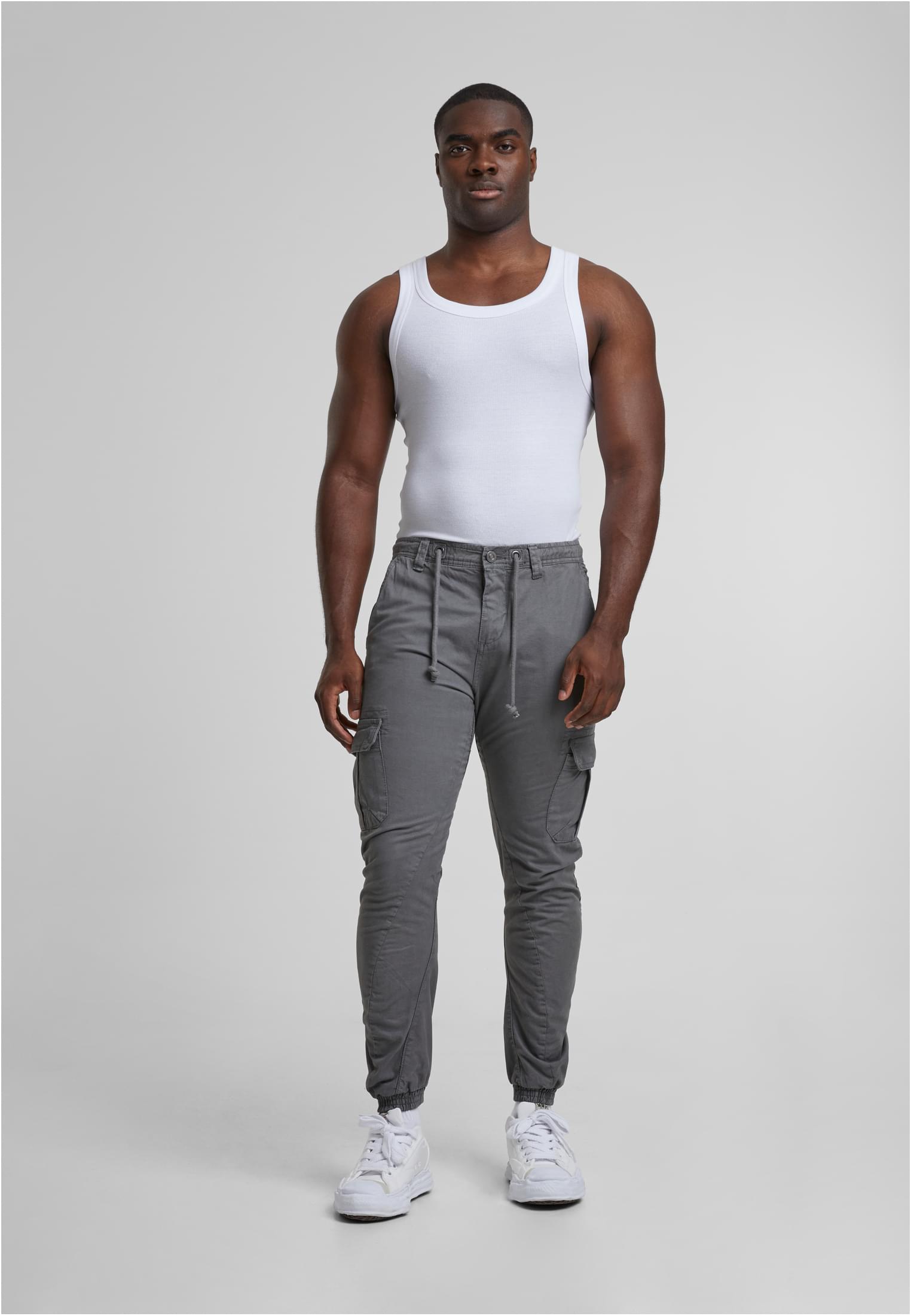 Helkroppsbild på en manlig modell som bär grå Cargo Jogging Pants, ett vitt linne och vita sneakers mot en ljusgrå bakgrund.