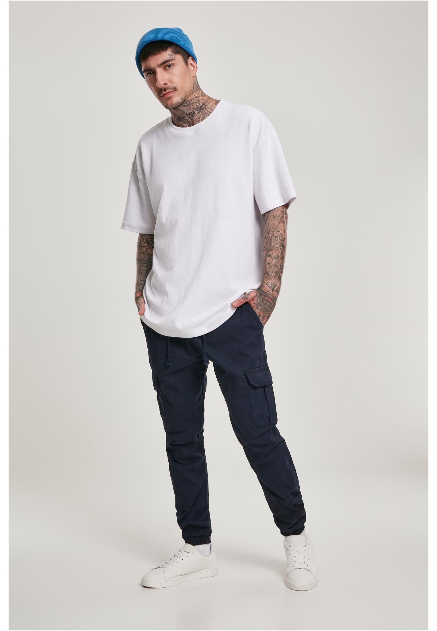 En man som bär mörkblå Cargo Jogging Pants, en vit t-shirt och en blå mössa.