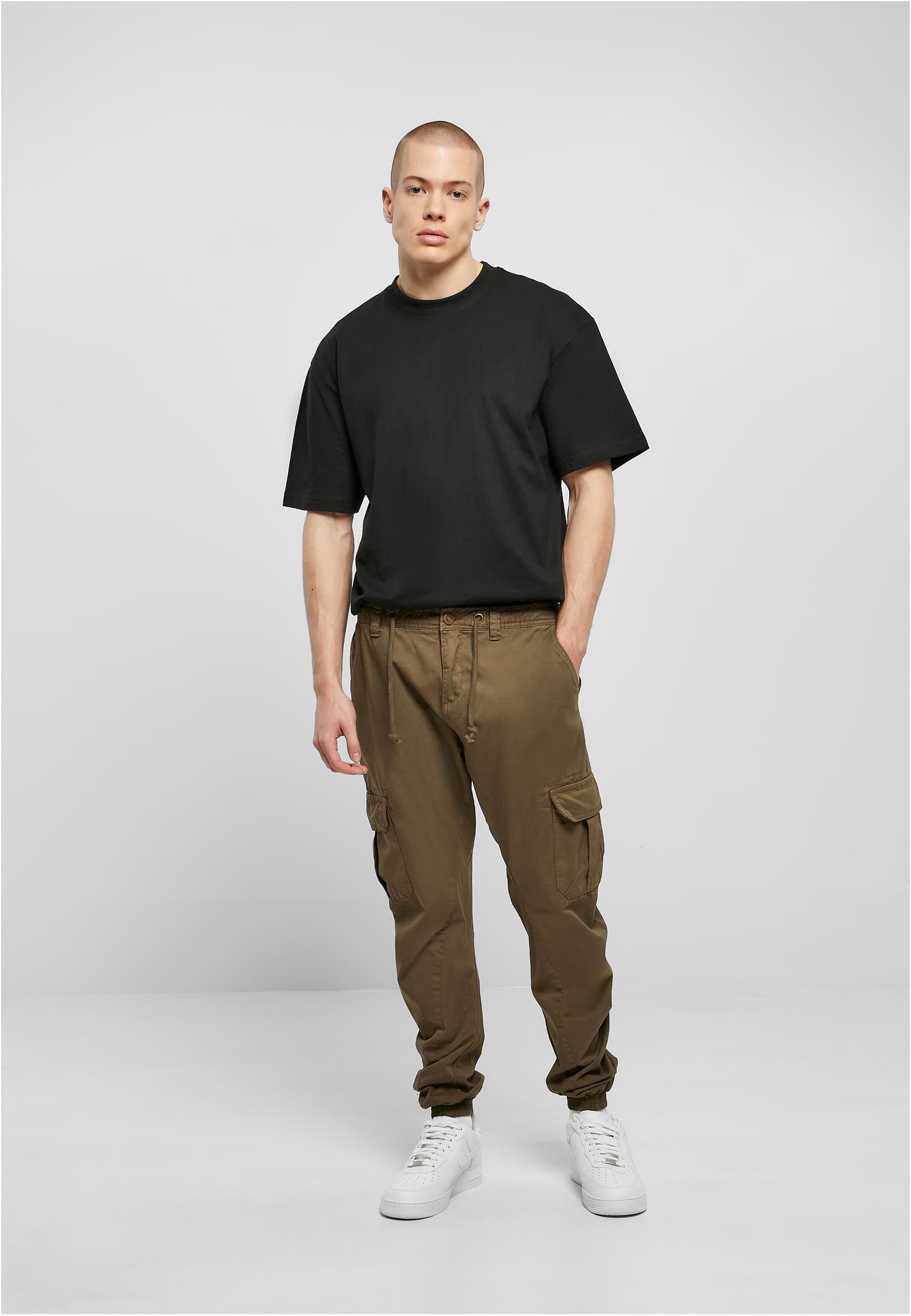 En man som bär ett par terracottafärgade UC Cargo Jogging Pants, en svart T-shirt och vita sneakers.