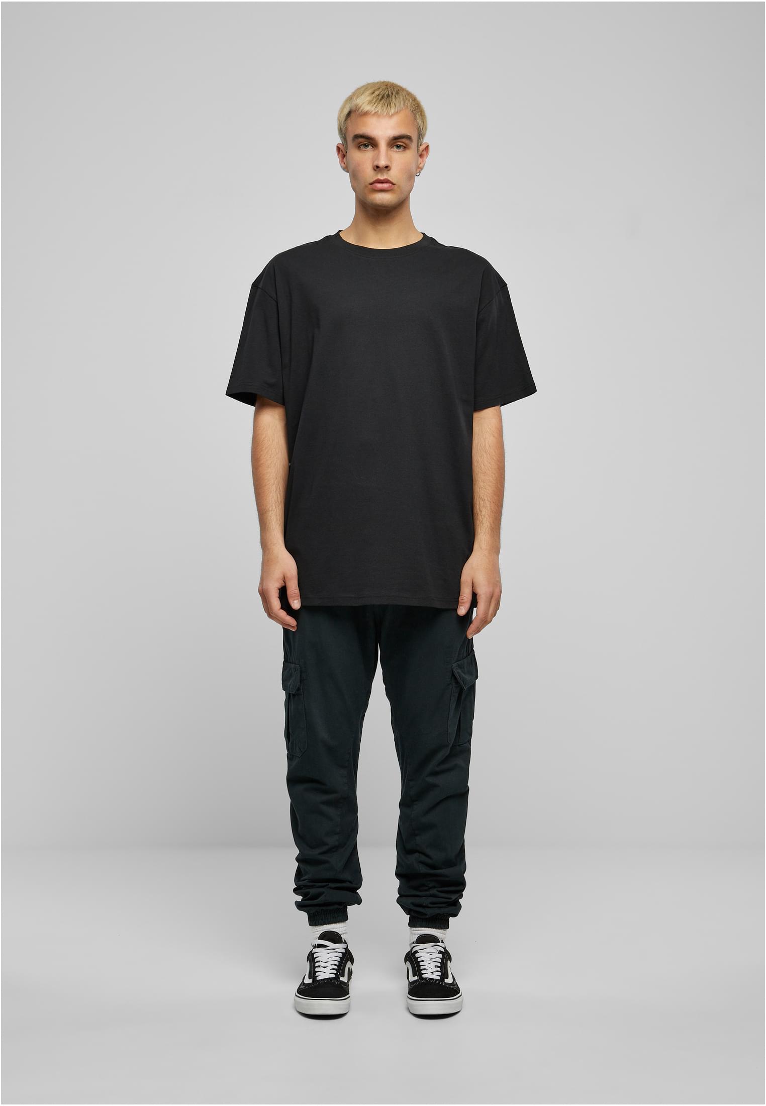 En manlig modell sedd framifrån, iklädd mörka cargo joggingbyxor, en svart t-shirt och sneakers mot en ljusgrå bakgrund.