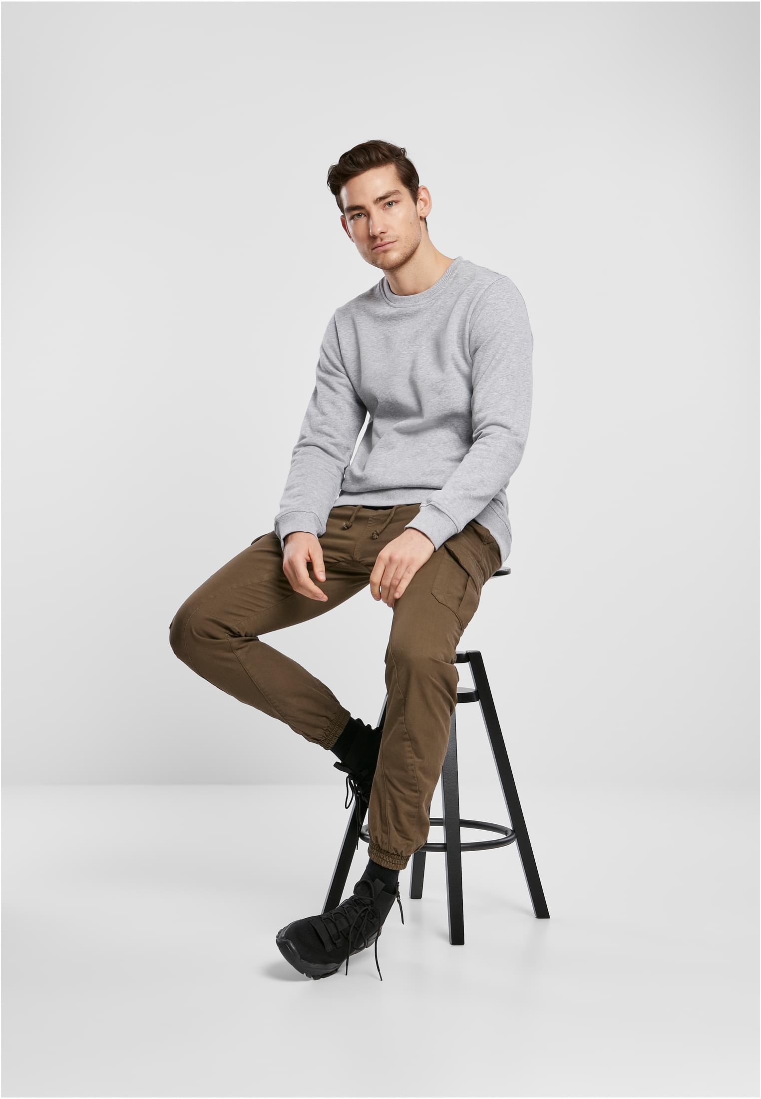 En manlig modell som sitter på en pall, klädd i terrakottafärgade cargo joggingbyxor och en grå sweatshirt.