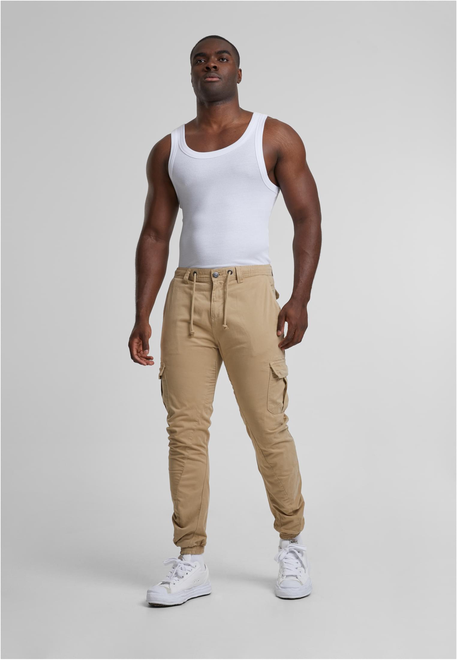Framifrån av en manlig modell som bär terrakottafärgade Cargo Jogging Pants, ett vitt linne och vita sneakers.