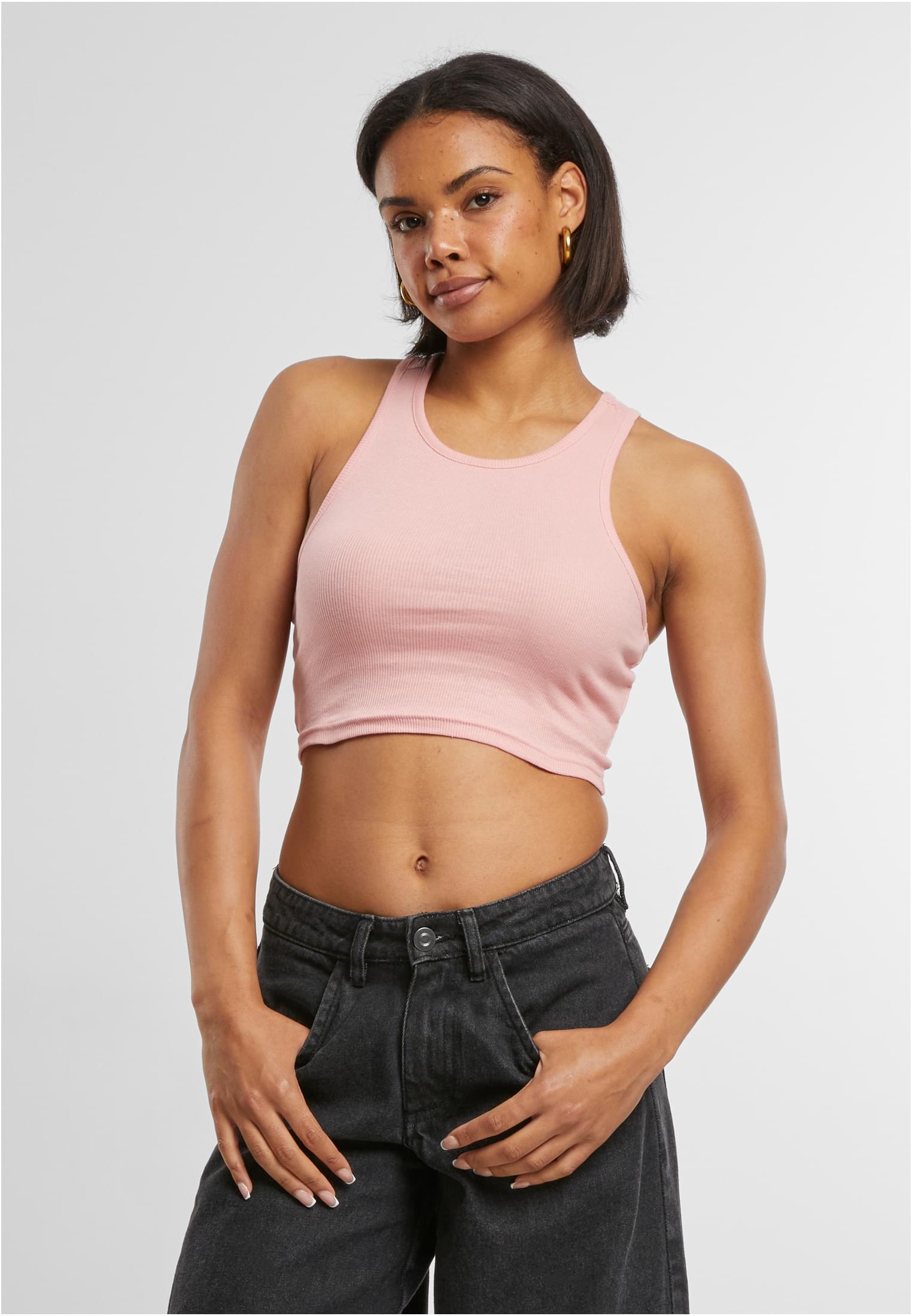 En kvinna som bär ett ljusrosa, ribbat och croppat linne tillsammans med svarta jeans, fotograferad framifrån.