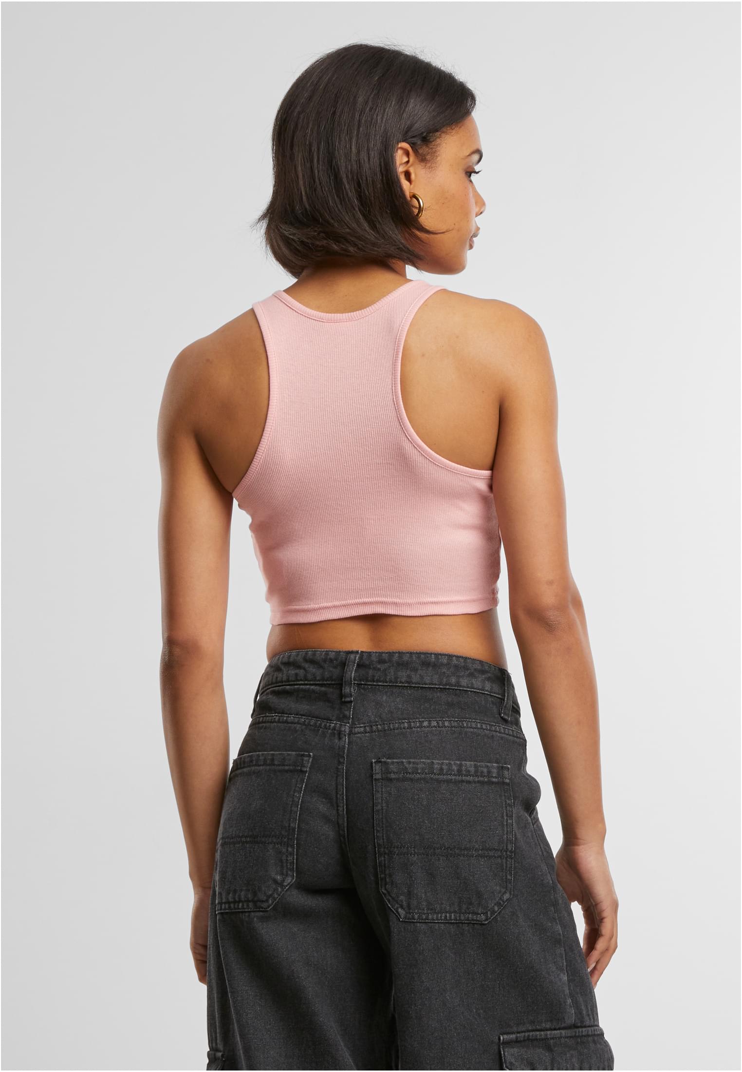 Kvinna sedd bakifrån som bär ett rosa, kort, ribbat linne och mörkgråa jeans.