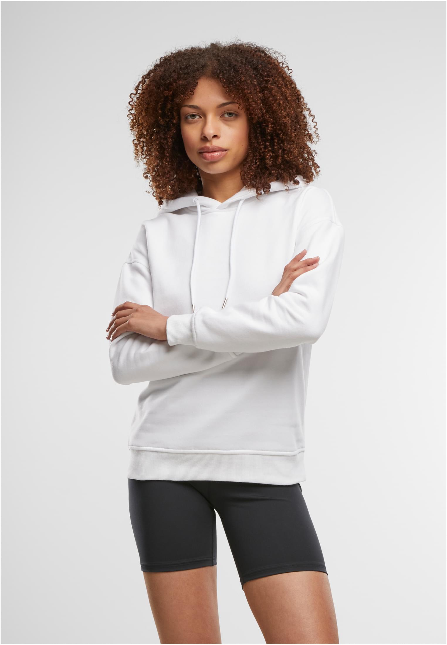 En kvinna poserar i en vit luvtröja och svarta cykelbyxor med armarna i kors.