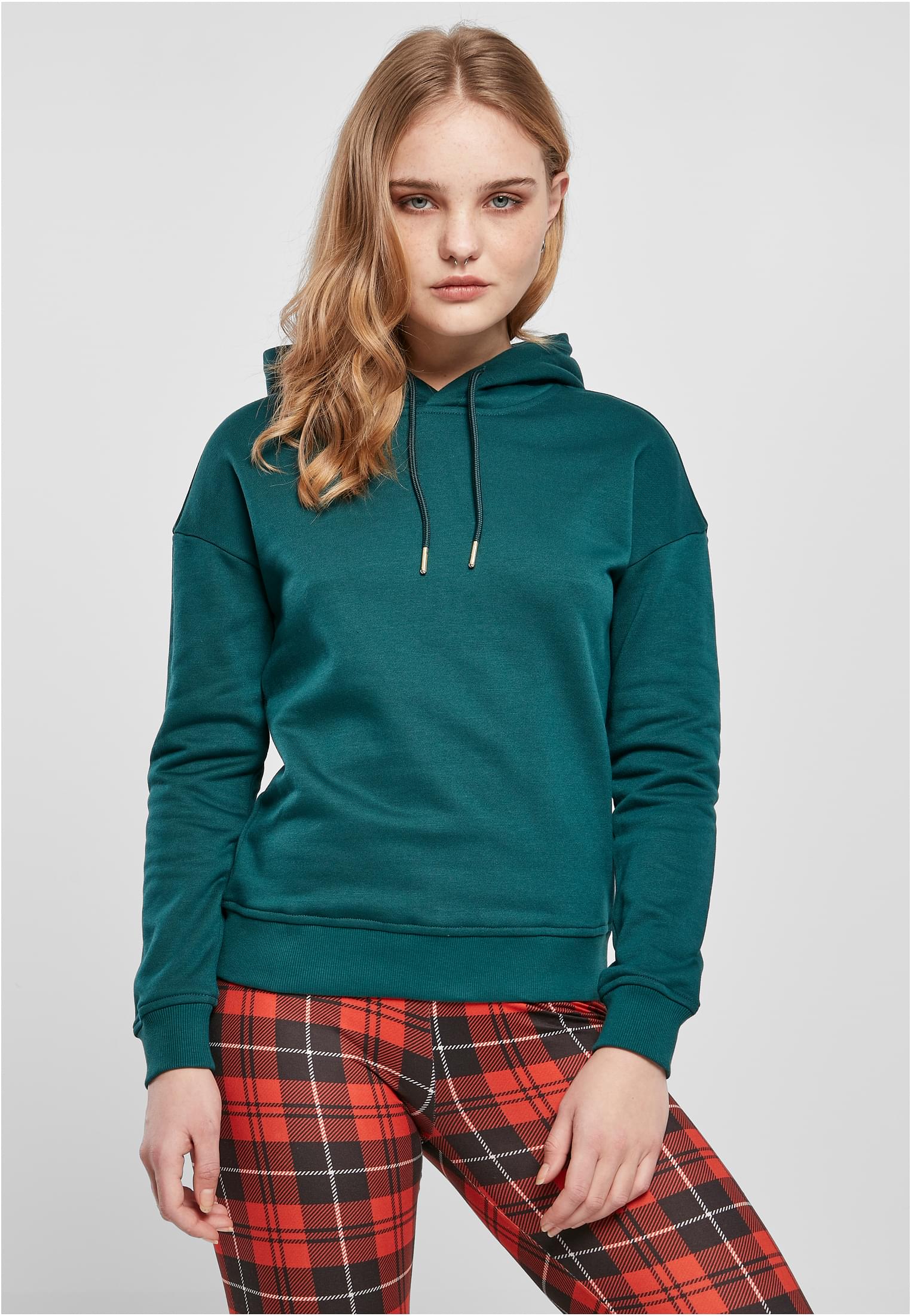 En kvinnlig modell som bär en grön UC Ladies Hoody och rödrutiga byxor.