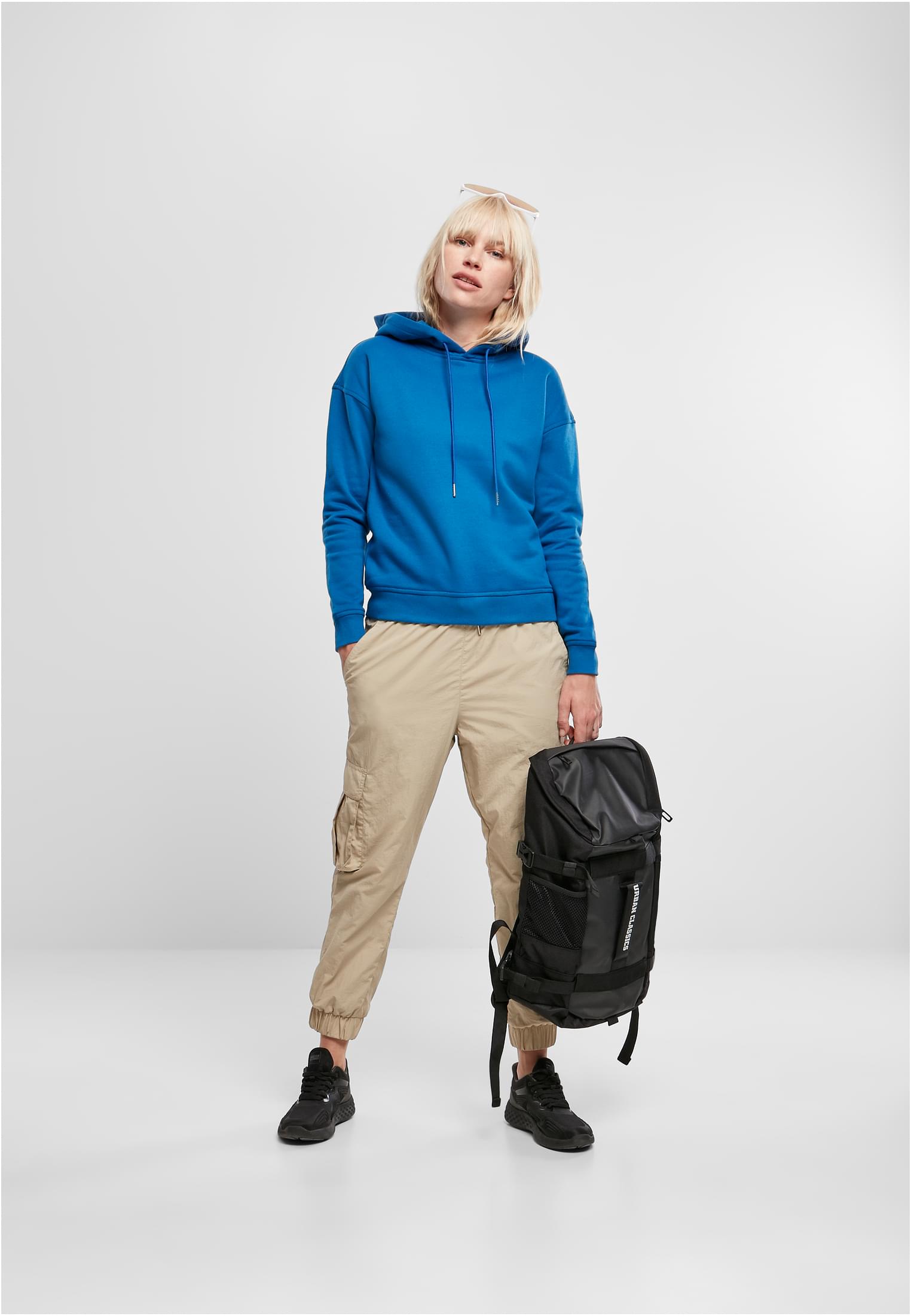 En kvinna som bär en blå Ladies Hoody, beiga cargobyxor och svarta sneakers, medan hon håller i en svart ryggsäck.