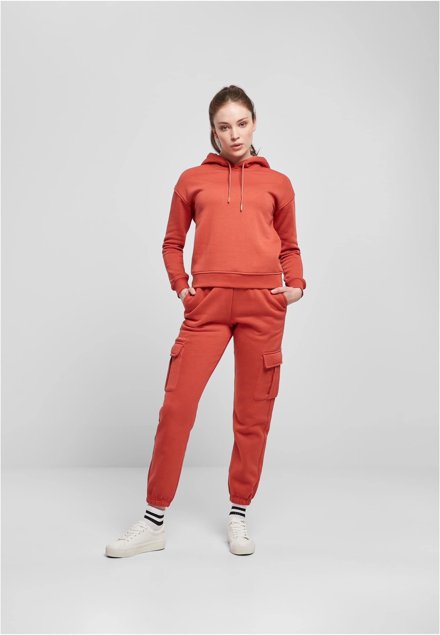En kvinna i helfigur som bär en roströd huvtröja och matchande mjukisbyxor i cargomodell.