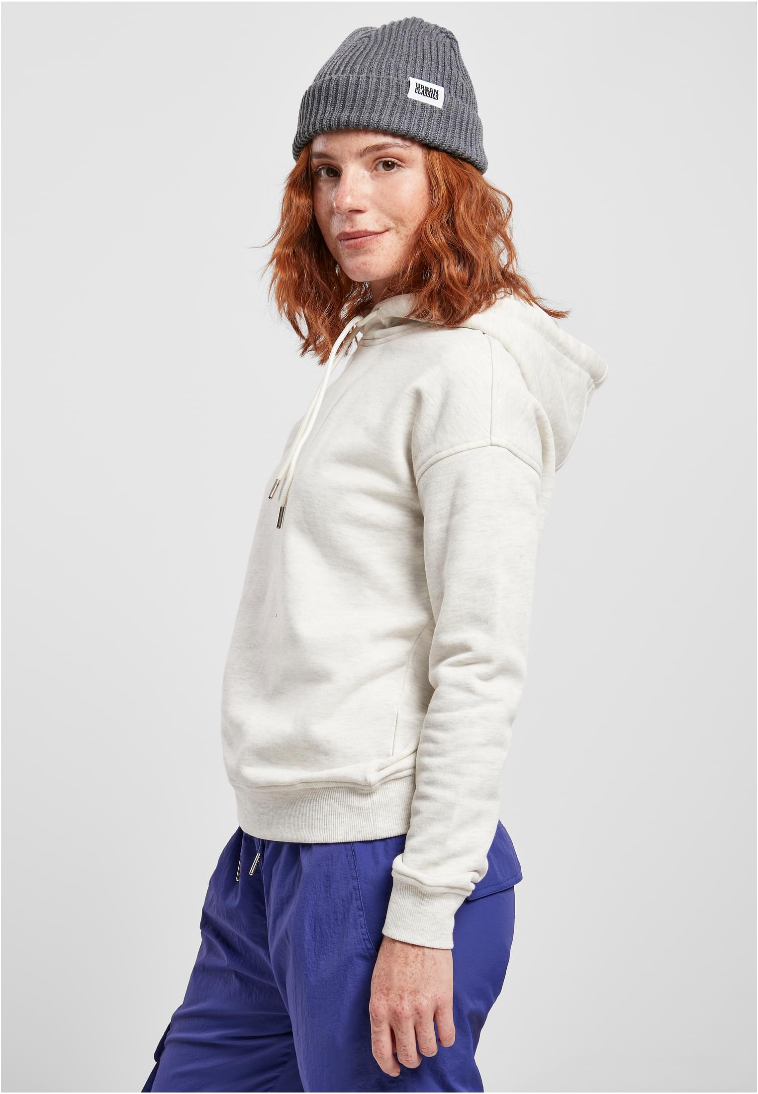 En kvinna, sedd från sidan, som bär en ljus huvtröja, blå byxor och en grå mössa.