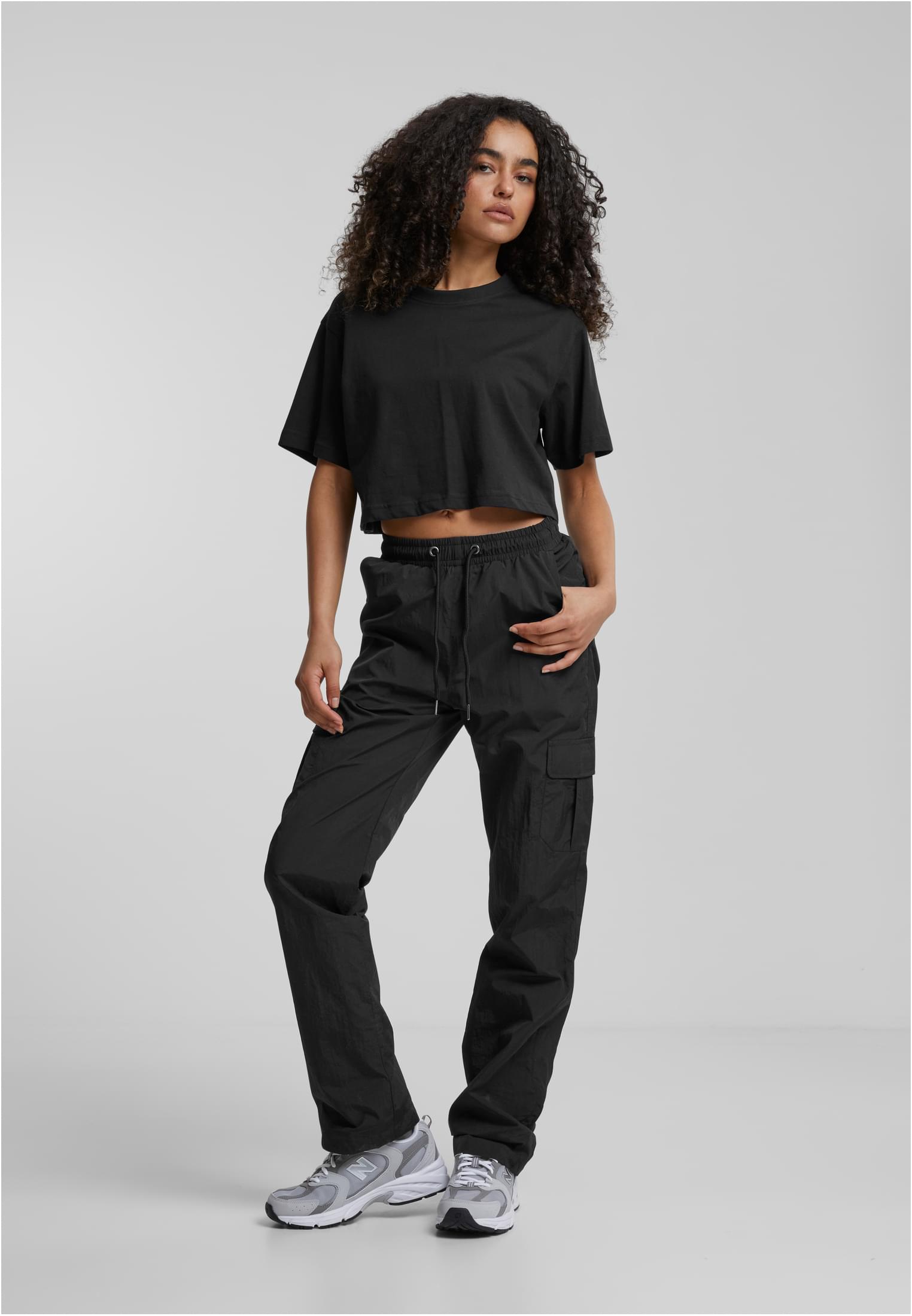 En kvinna som visar upp Ladies Short Oversized Tee i svart, tillsammans med svarta cargobyxor.