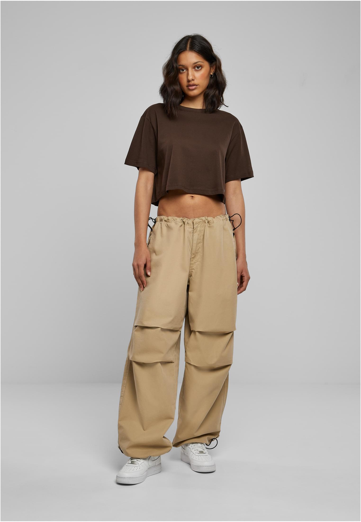 En kvinna fotograferad framifrån i en kort, oversized t-shirt i terrakotta, pösiga beiga cargobyxor och vita sneakers.