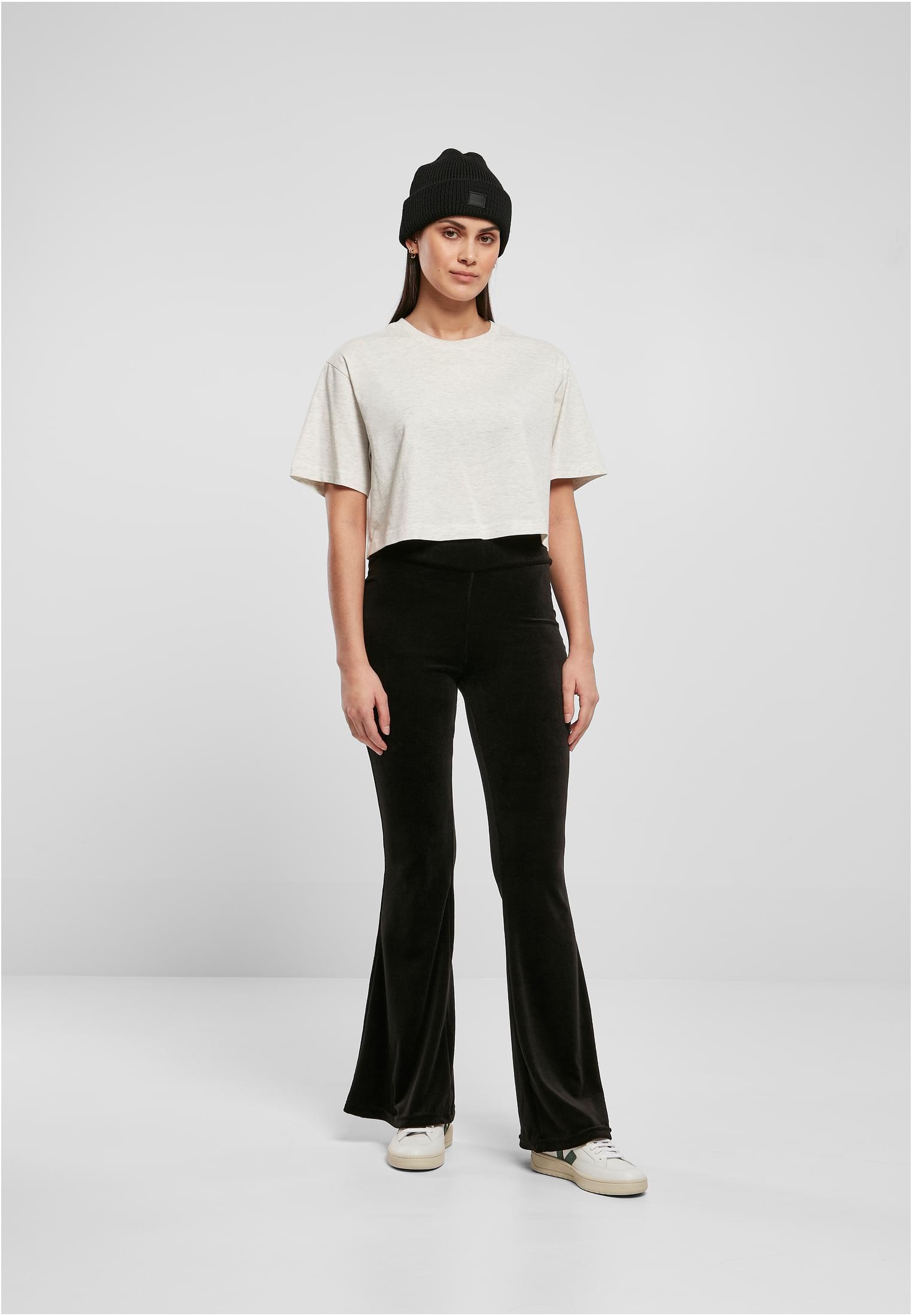 En kvinnlig modell som bär en kort, oversized t-shirt i ljus färg, svarta utsvängda byxor och en svart mössa.