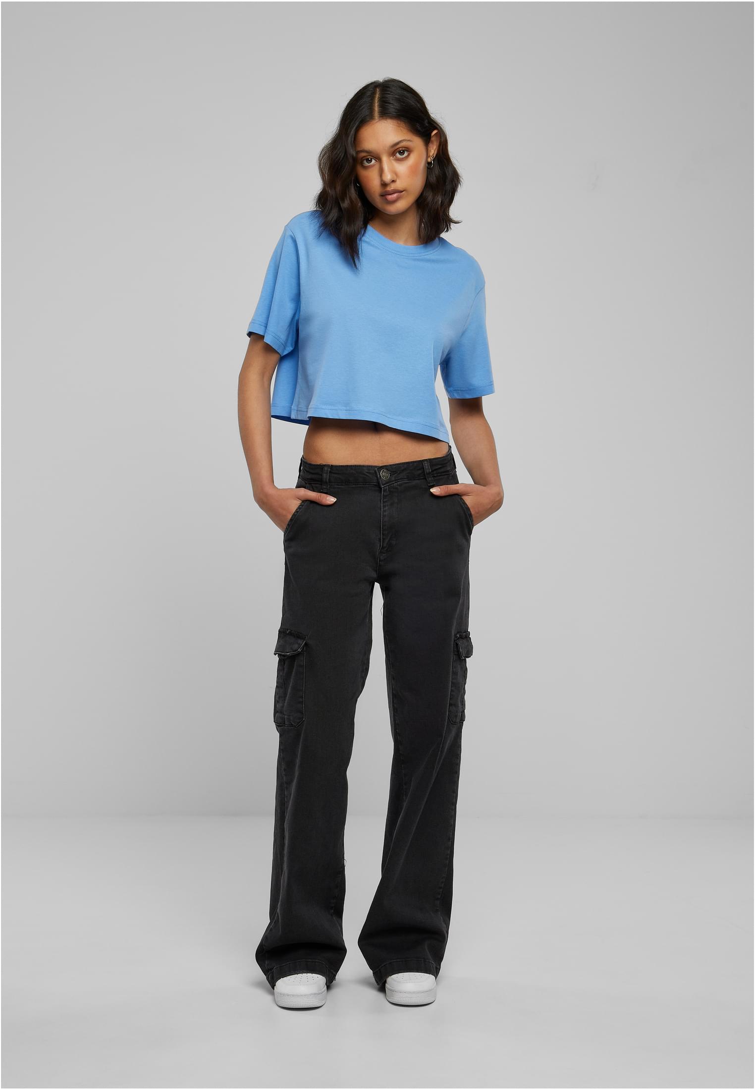 En modell i helfigur som bär en kort, oversized ljusblå t-shirt och svarta cargobyxor med vida ben.