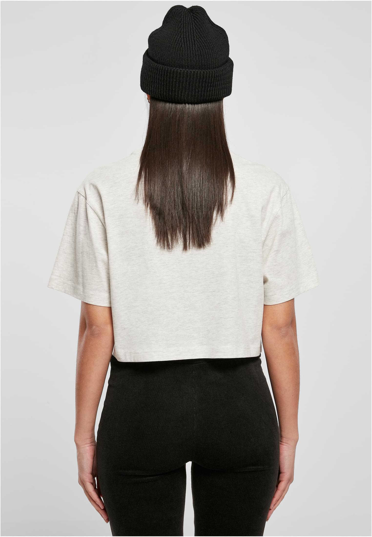 Kvinna sedd bakifrån, iklädd en ljusgrå Ladies Short Oversized Tee, svarta byxor och en svart mössa.